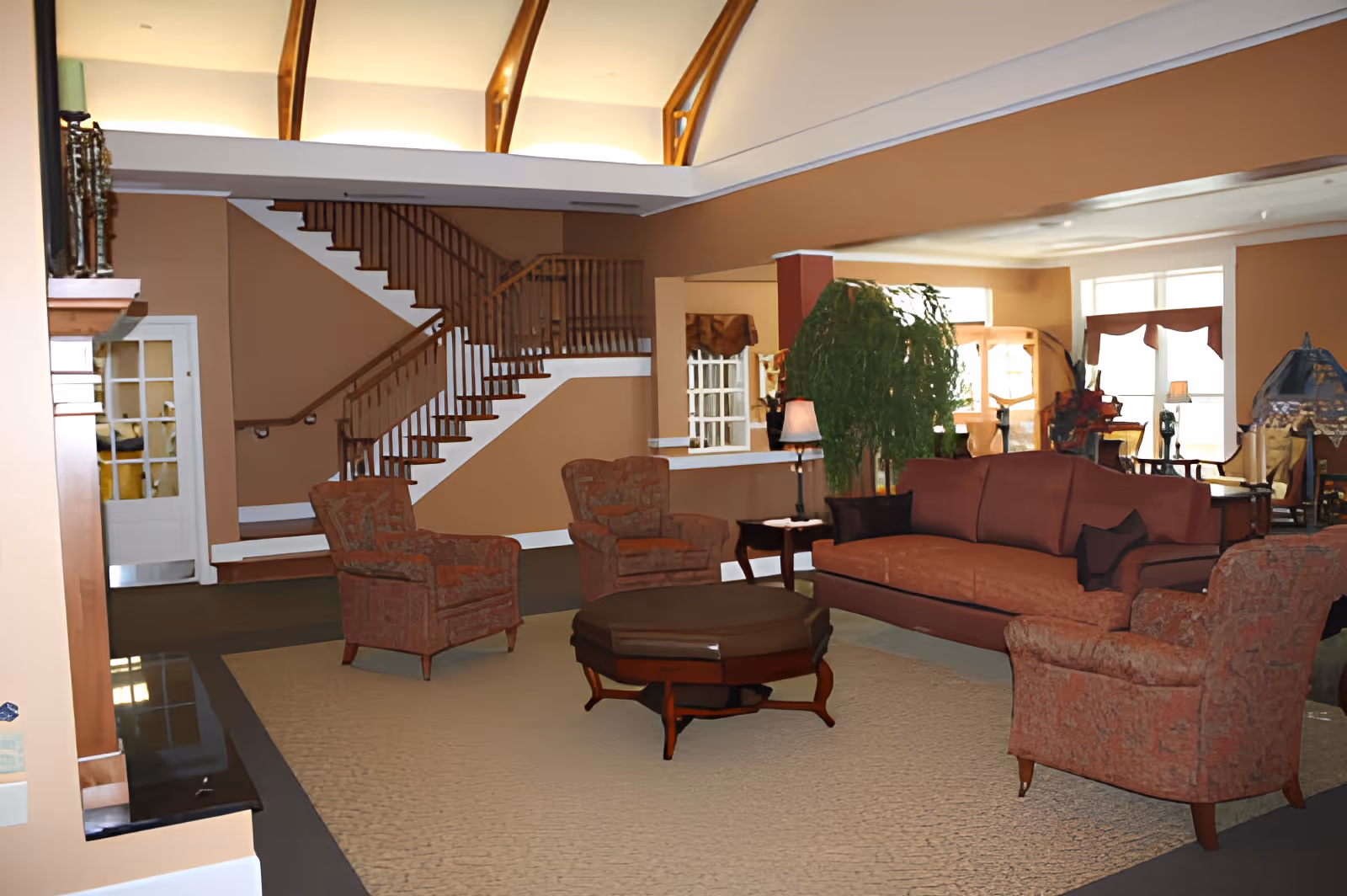 Spacious communal living room with sofas, armchairs, a central coffee table, potted plant and a staircase in the background.