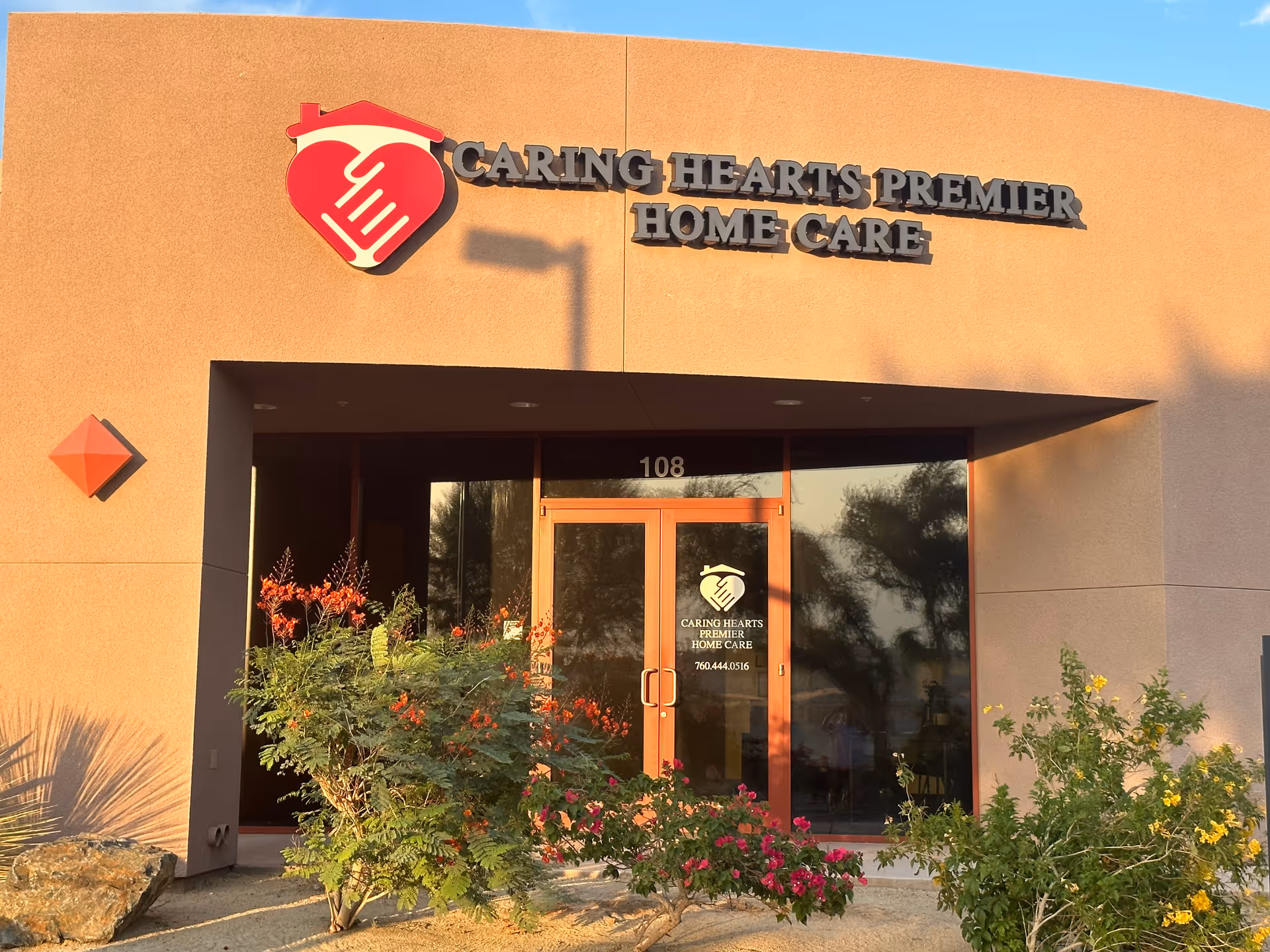 Orange stucco building entrance with Caring Hearts Premier Home Care sign and glass doors.