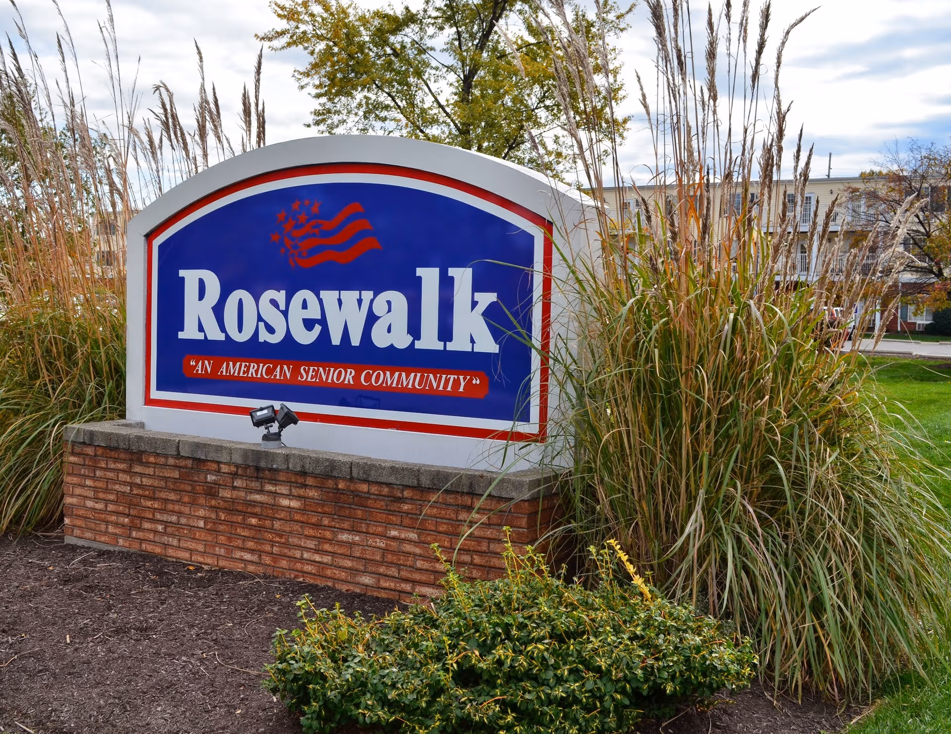 Large Rosewalk sign with blue panel and red trim, set among tall grasses.
