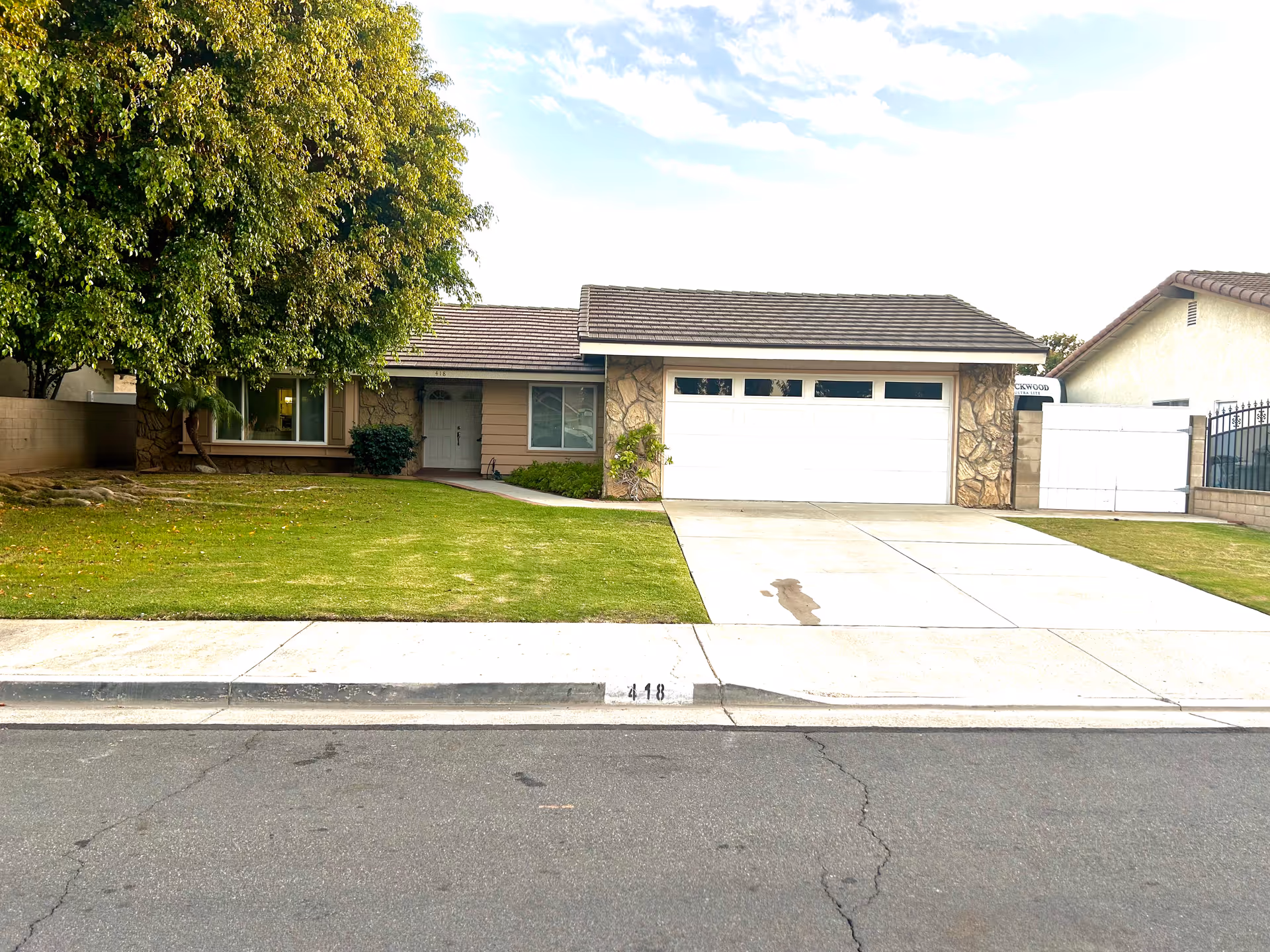 Single-story house front with a two-car garage, driveway, lawn and a large tree.