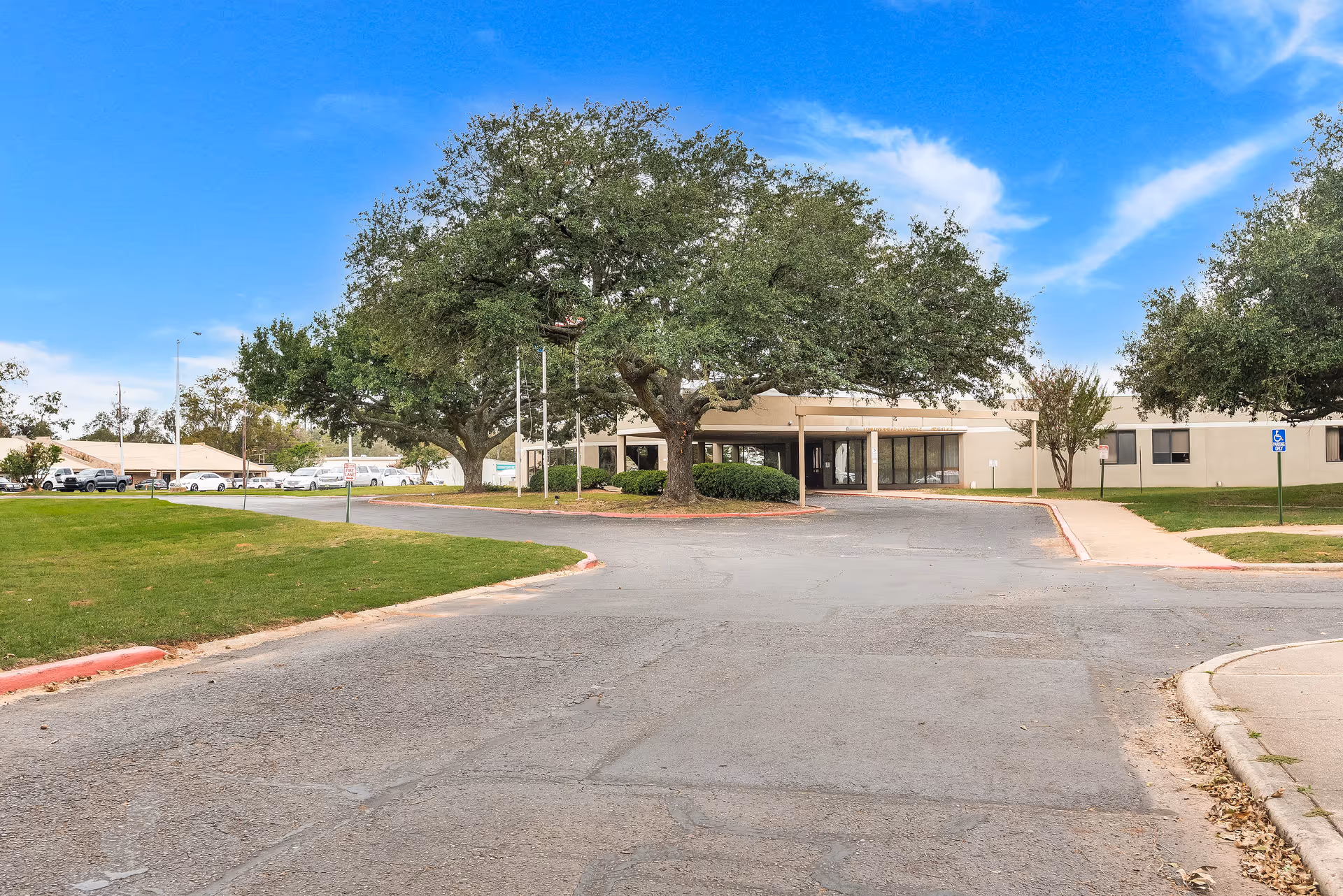 Exterior view of a single-story senior care building with driveway, trees, and parking.