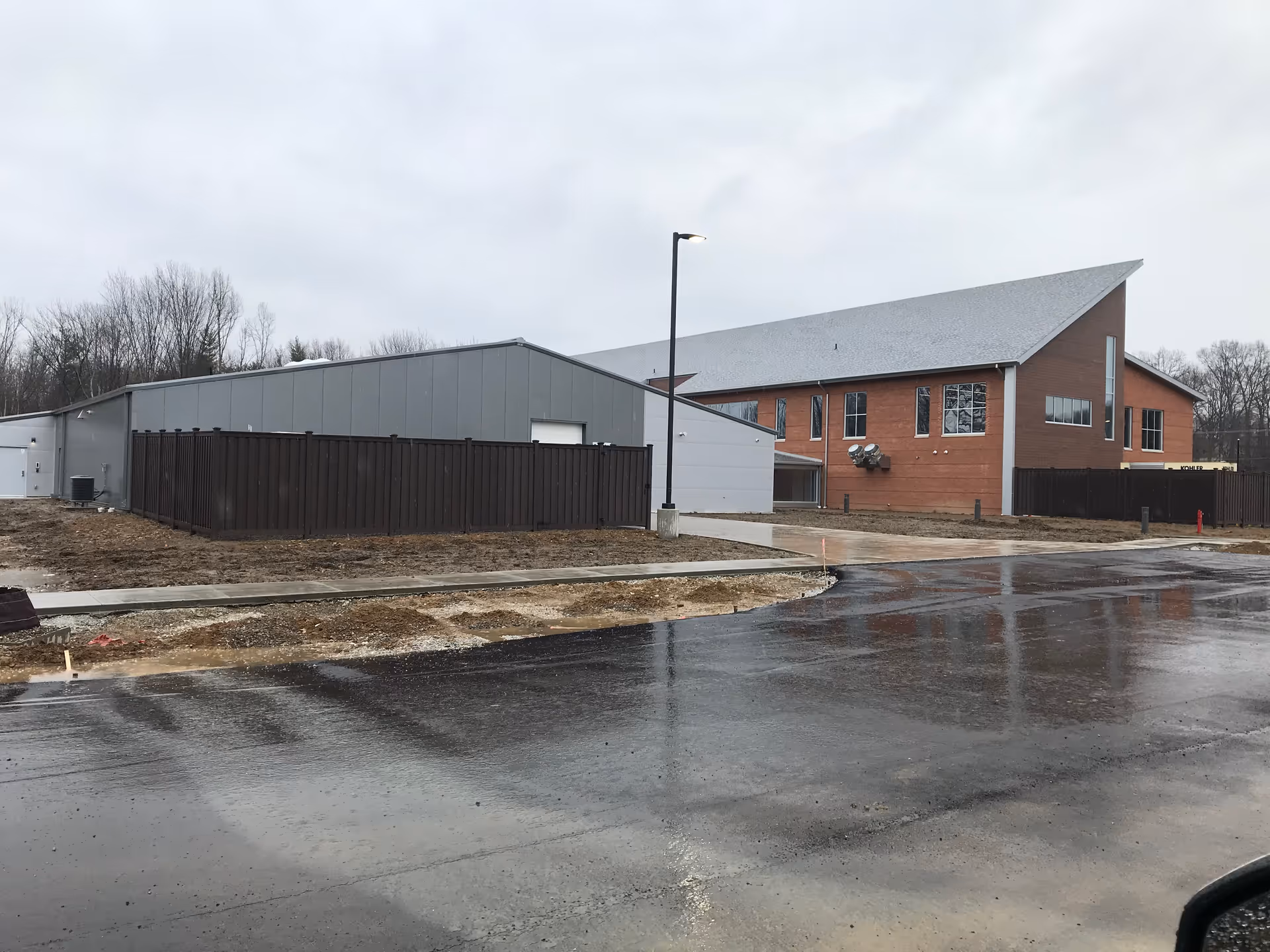 Newly built senior living facility with brick main building and gray annex beside a wet street.