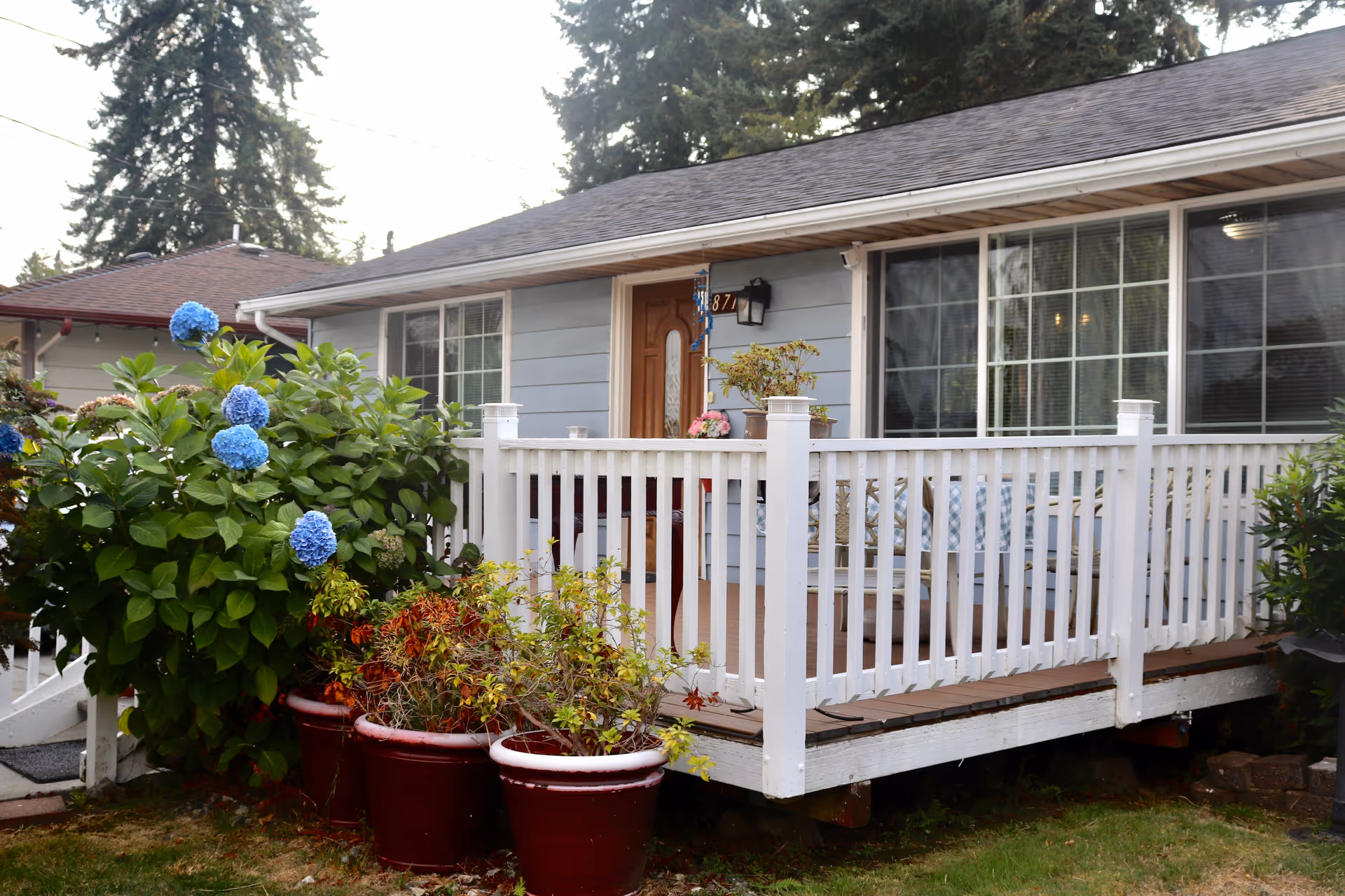 Front view of a single-story home with a white railing deck and potted plants.