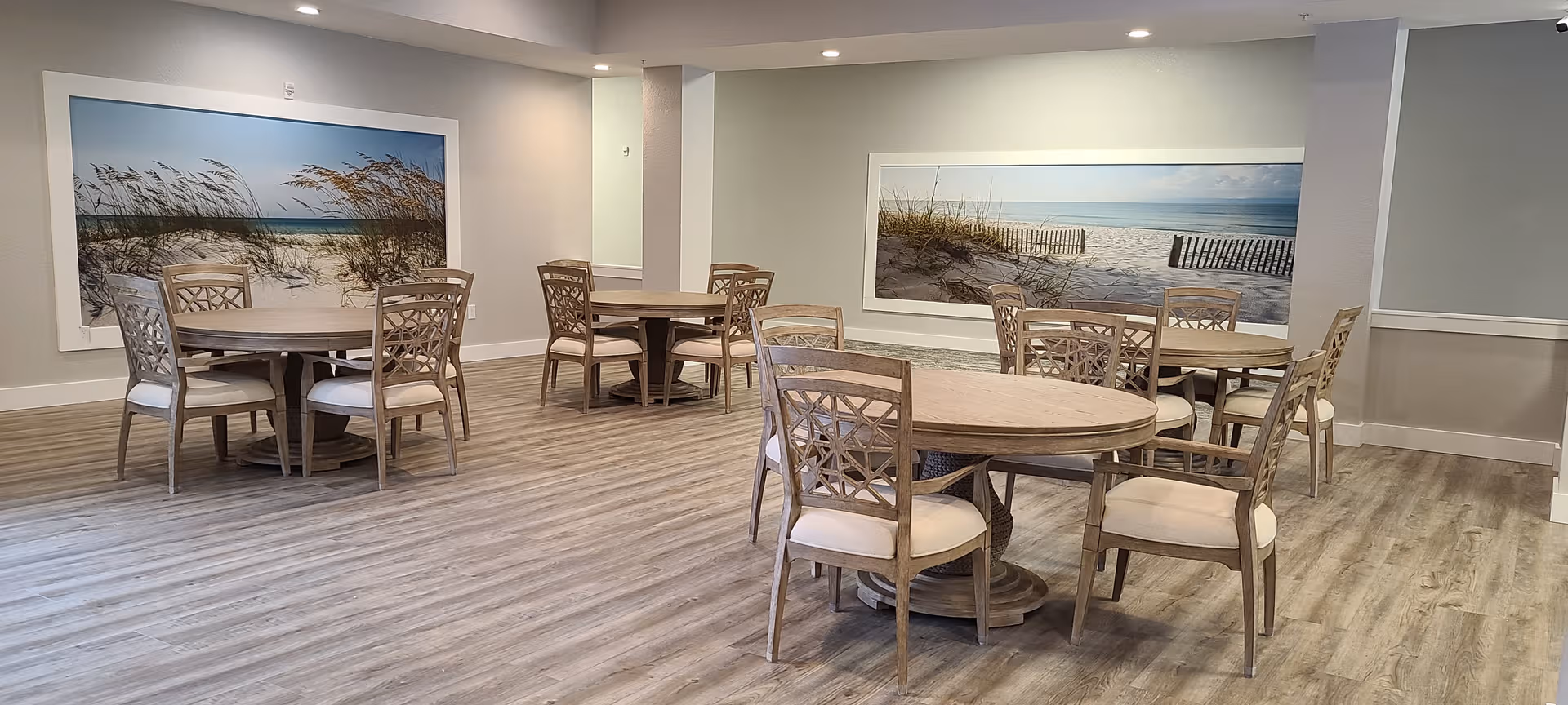 Bright dining area with round tables, beige chairs, and beach-themed wall art.
