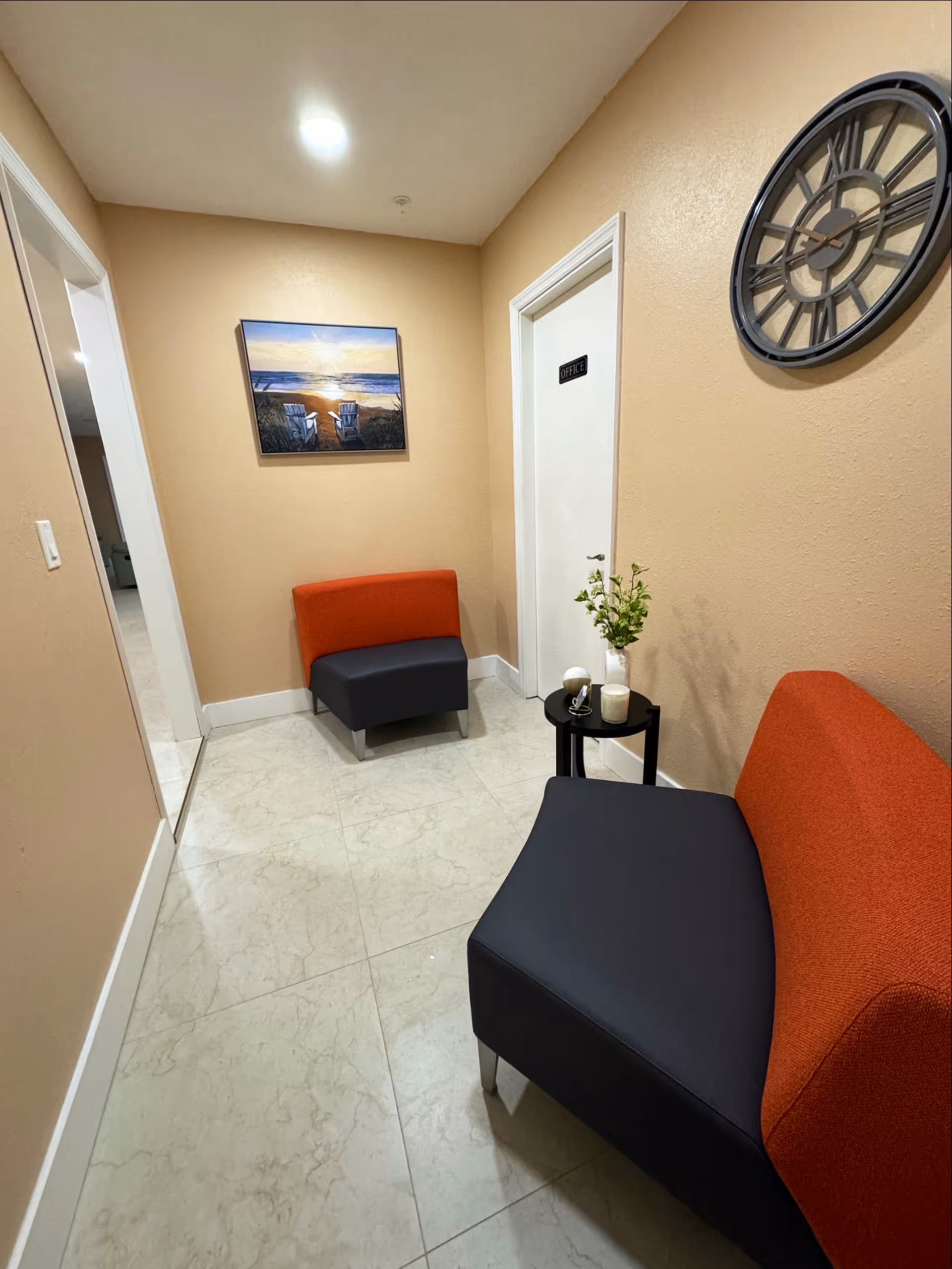 Beige-walled waiting area with orange and navy seating and an office door.