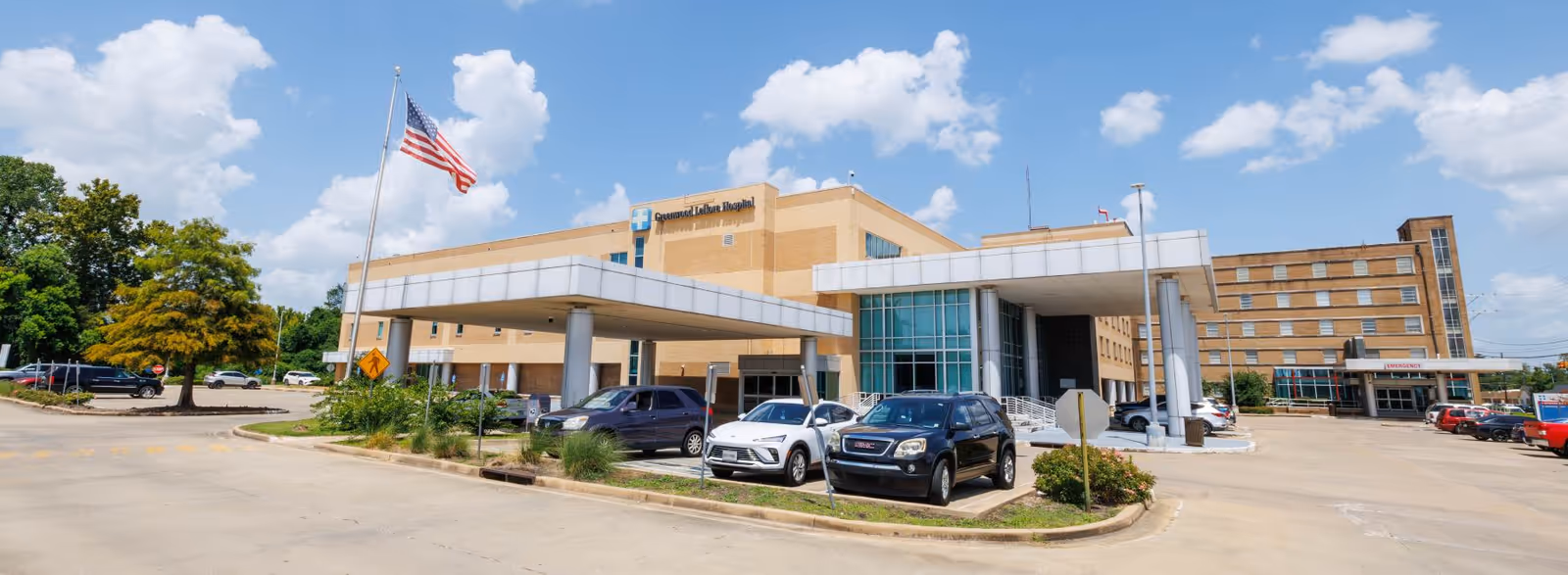 Front view of Greenwood Leflore Hospital building with parked cars and flag.