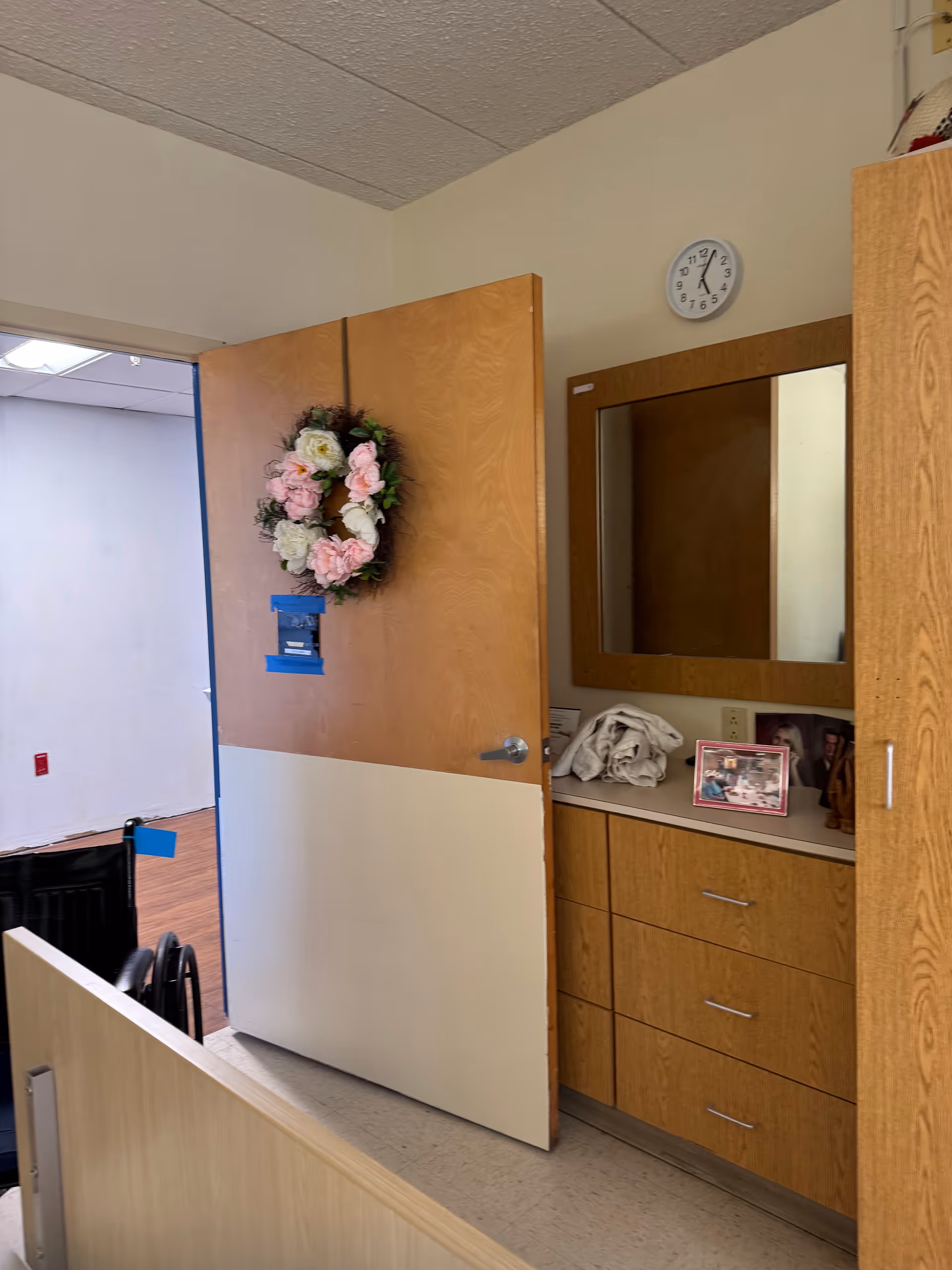 Interior hallway with wooden cabinets, a mirror, wreath on a door, and a clock.