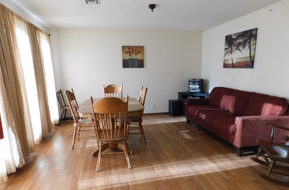 A bright living-dining room with a wooden table and chairs, a red sofa, hardwood floors, and wall art.
