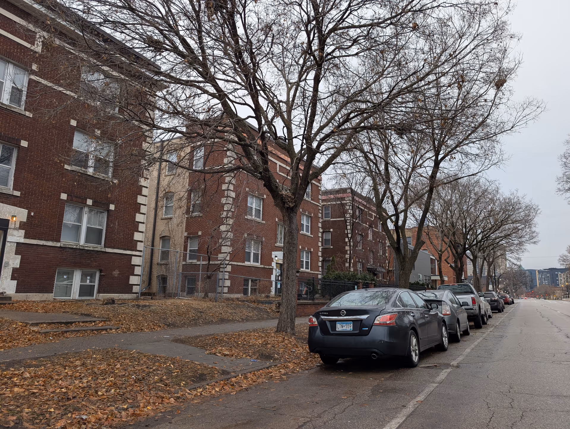 Brick multi‑story residential buildings and leafless trees along a street with parked cars.