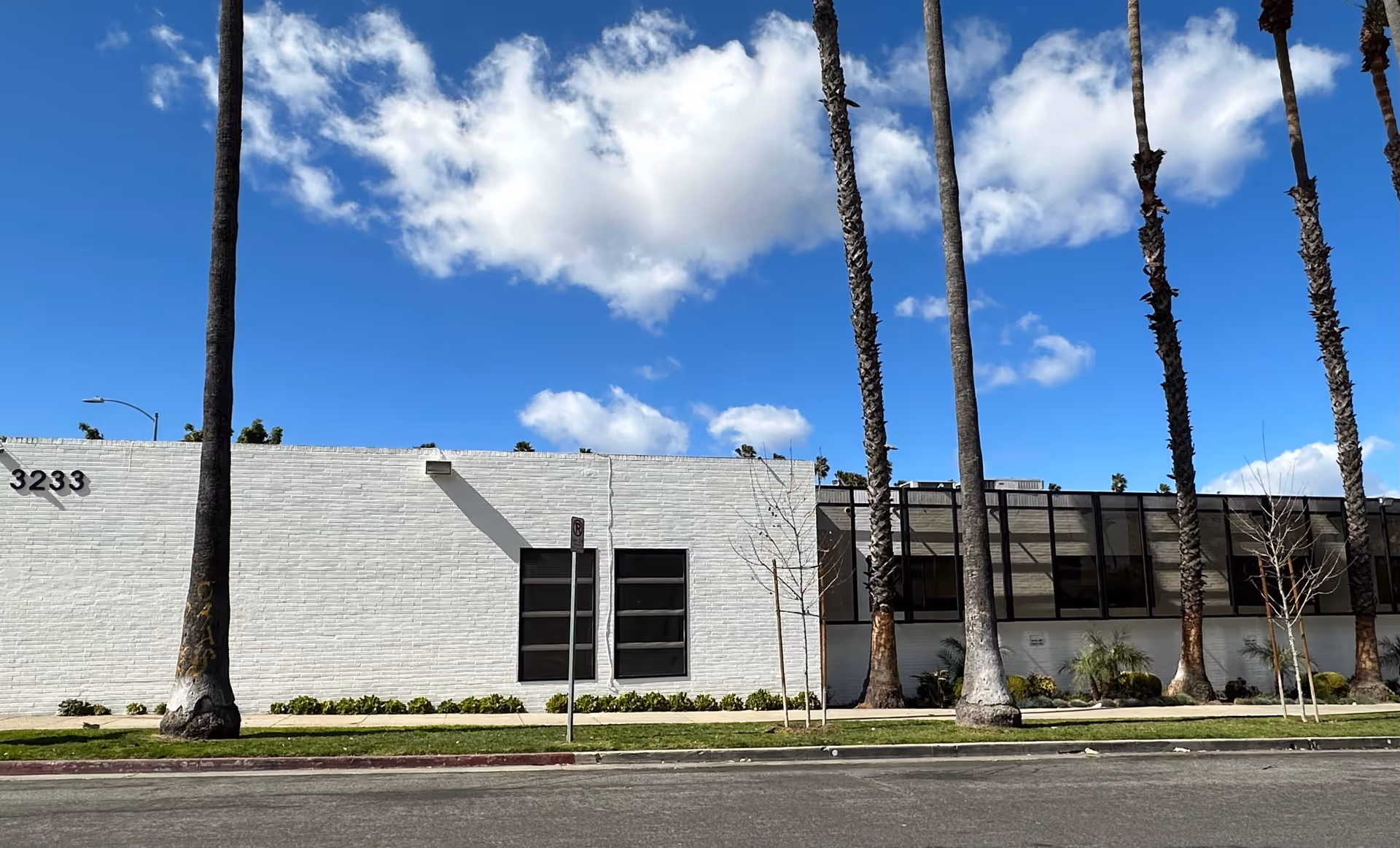 Exterior view of a white senior living facility with tall palm trees along the sidewalk.
