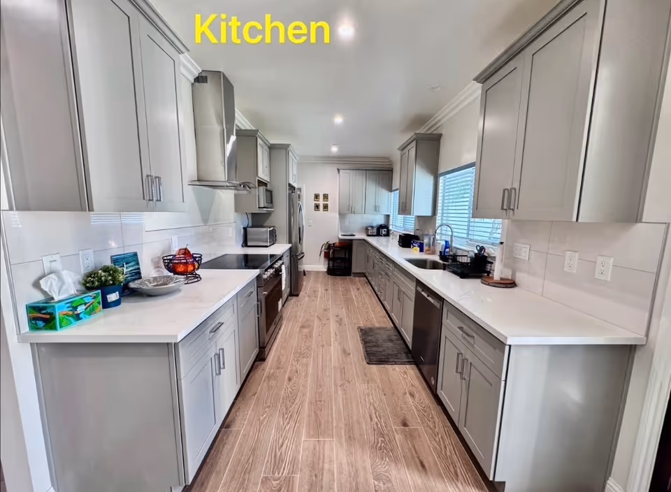 Long galley kitchen with gray cabinets, white countertops, and stainless steel appliances.