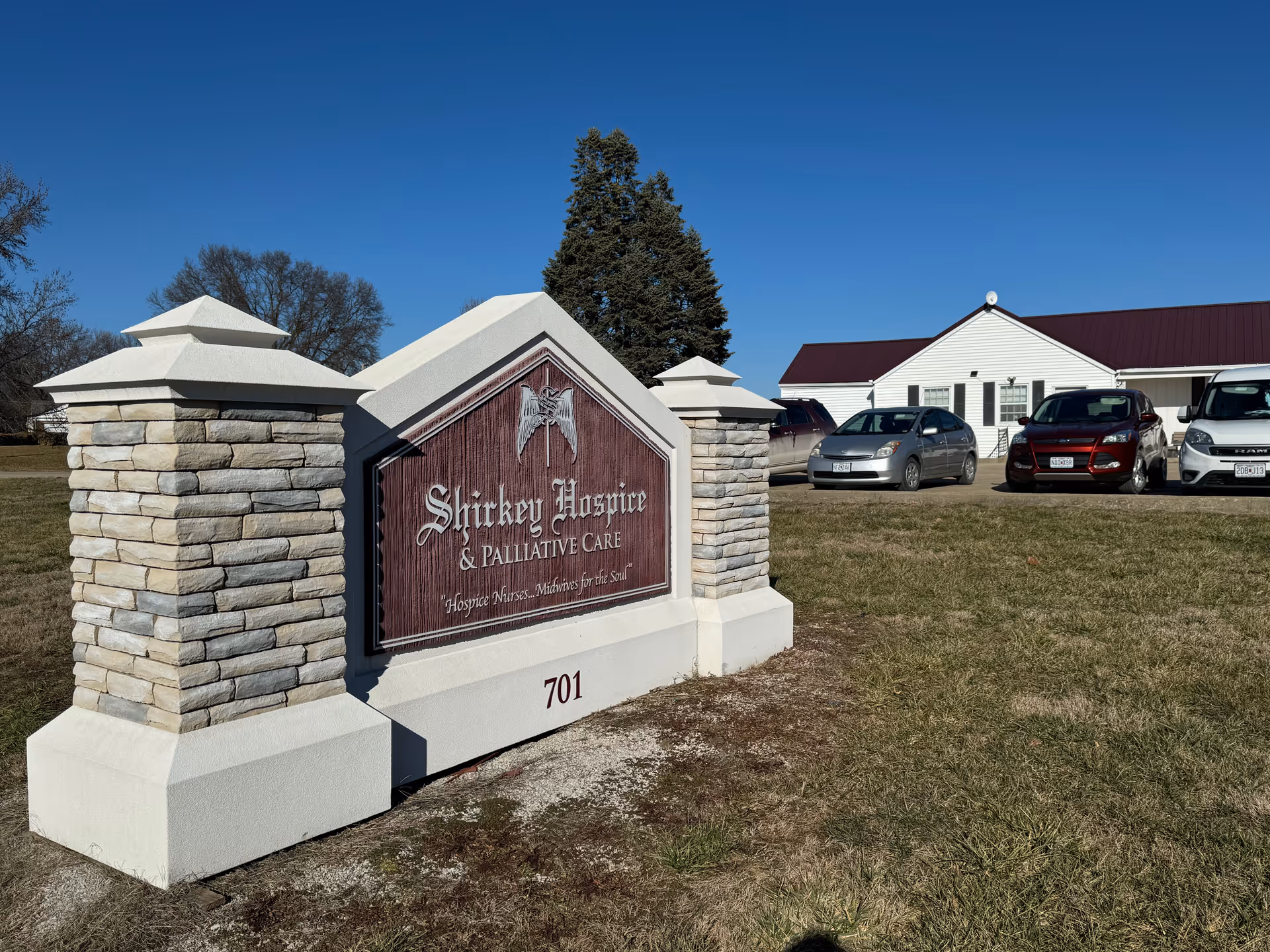 Exterior view of Shirkey Hospice & Palliative Care sign with parked cars and building in background
