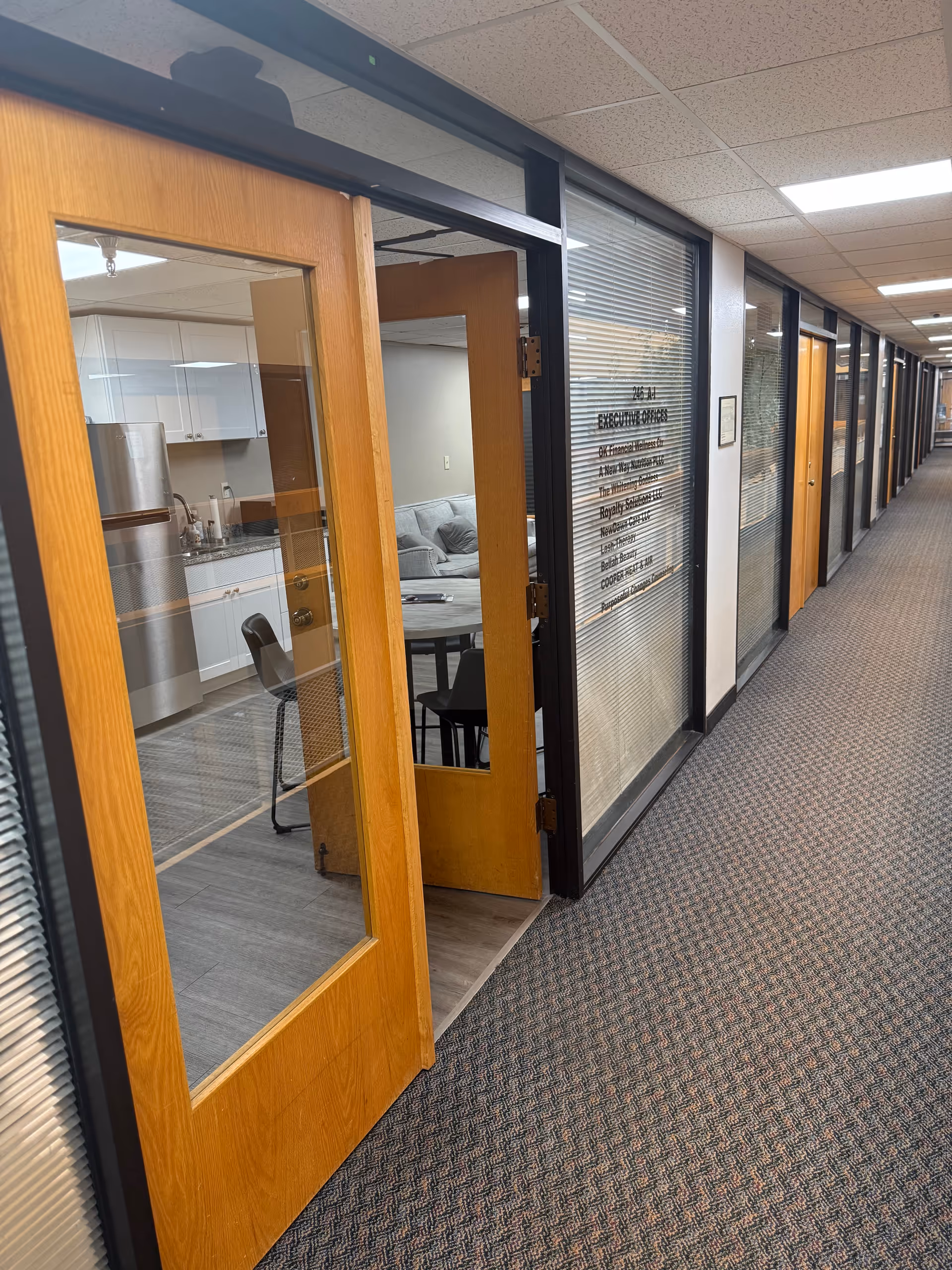Long hallway of a senior living facility with wood-framed glass doors and a visible kitchenette.