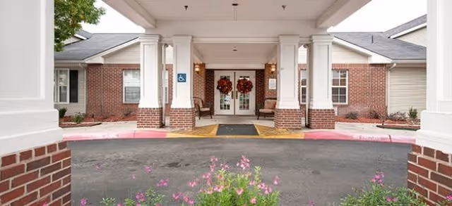 Brick building entrance with white columns, wreaths, and a covered portico.