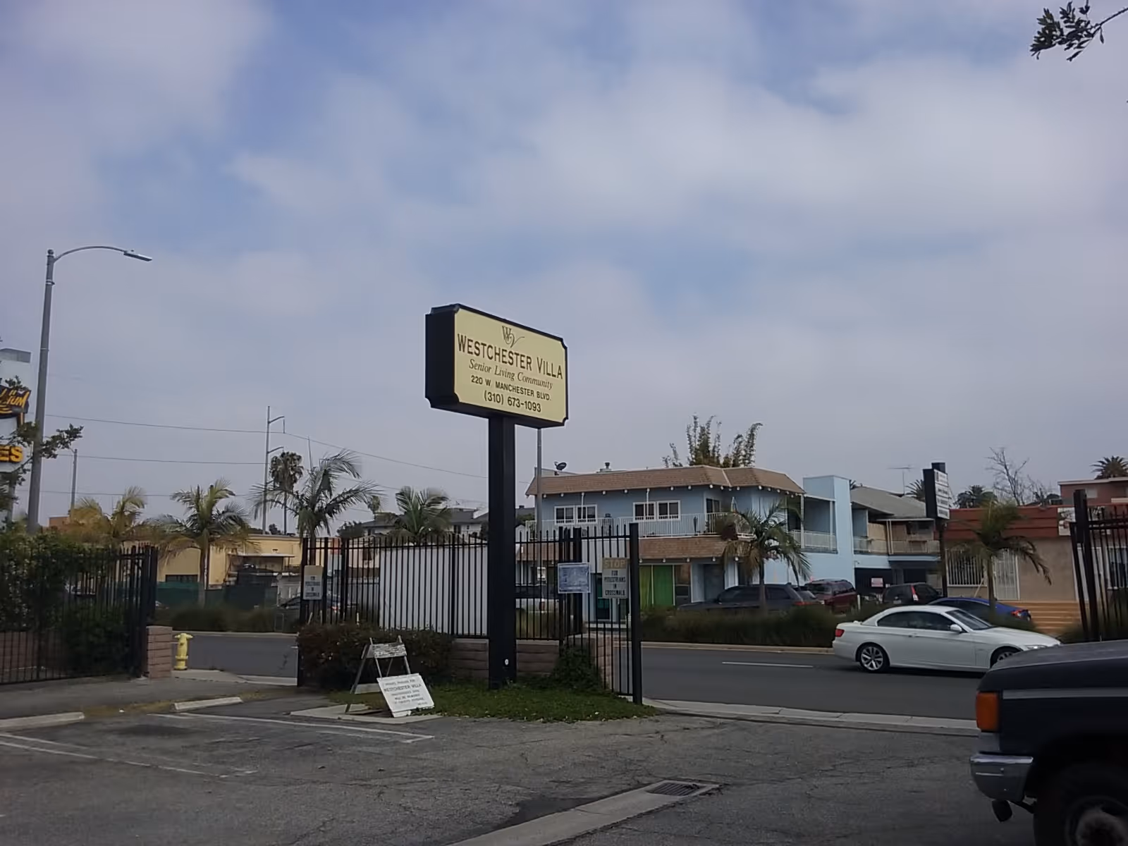 Gated exterior view of Westchester Villa senior living campus with sign and street.