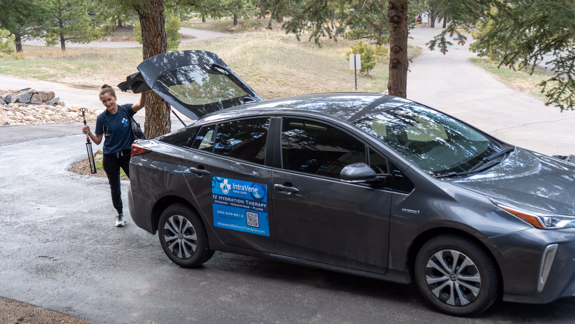 A mobile IV therapy car parked outdoors with a worker by the open trunk.