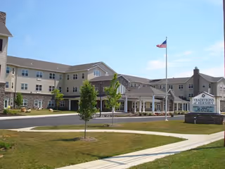 Exterior view of Traditions of Hershey senior living facility with driveway, lawn, and flagpole.