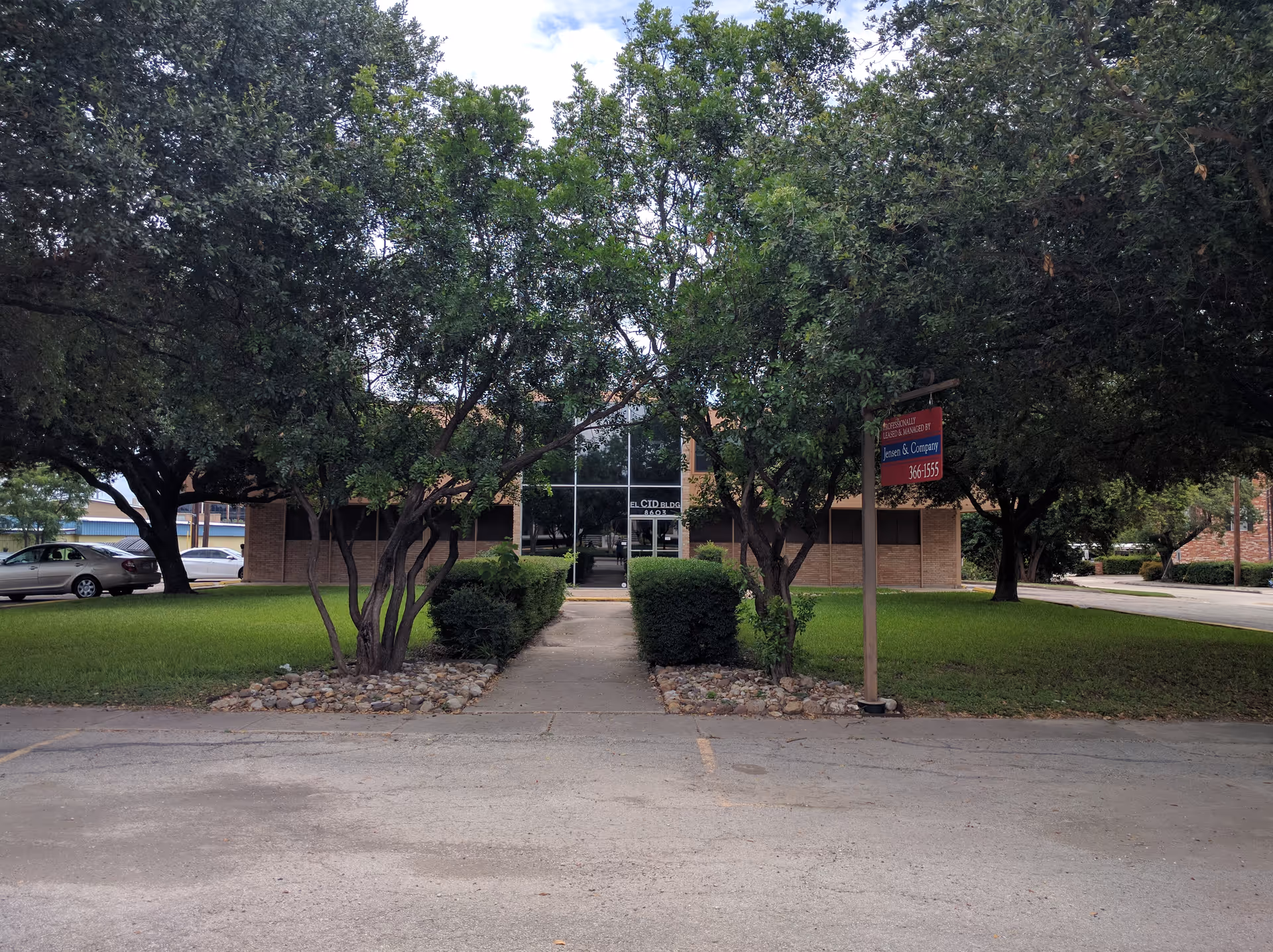 Front entrance of a brick senior living facility with glass doors, surrounded by trees.