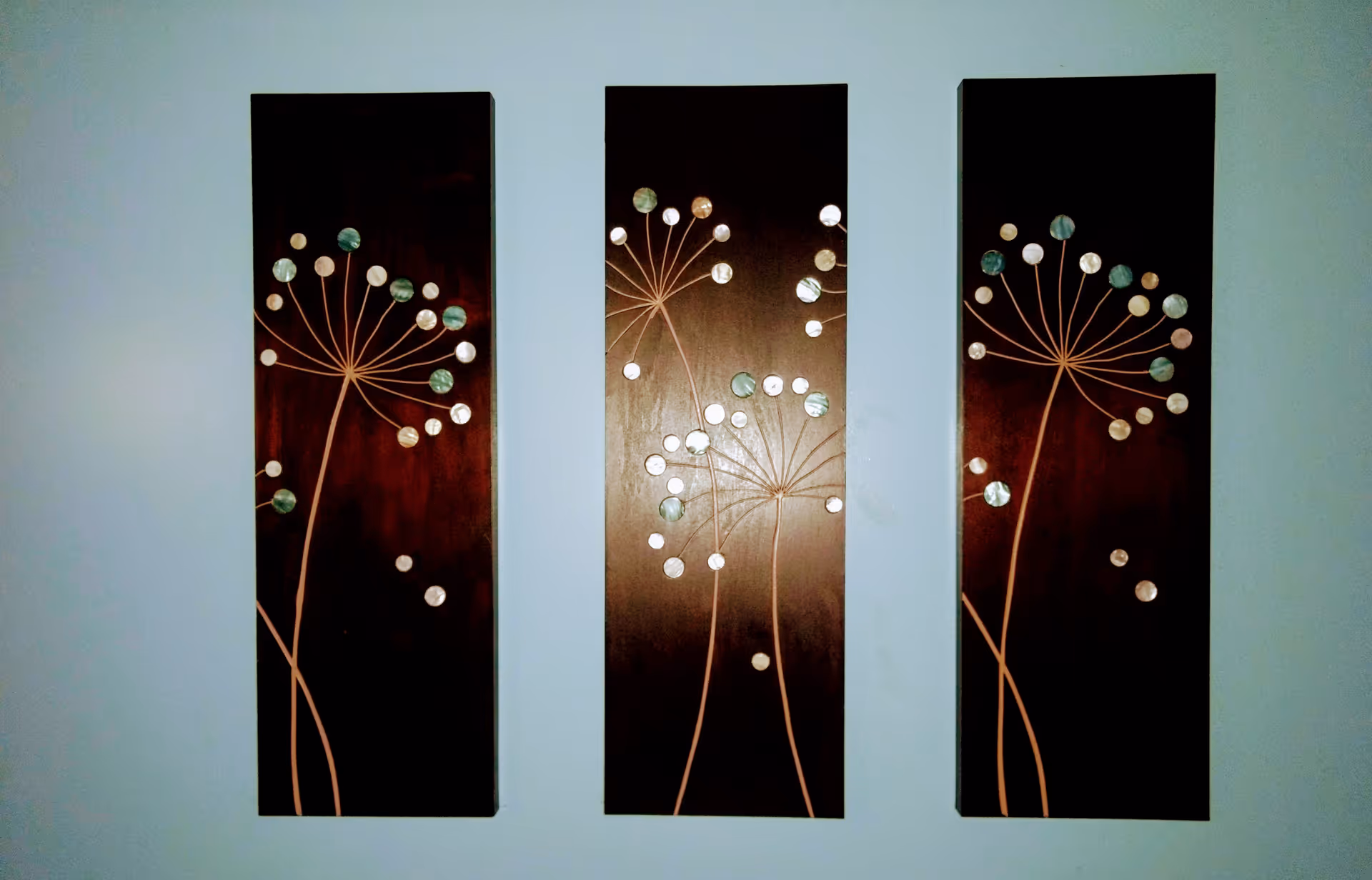 Three vertical panels featuring abstract dandelion-like designs hang on a pale wall.