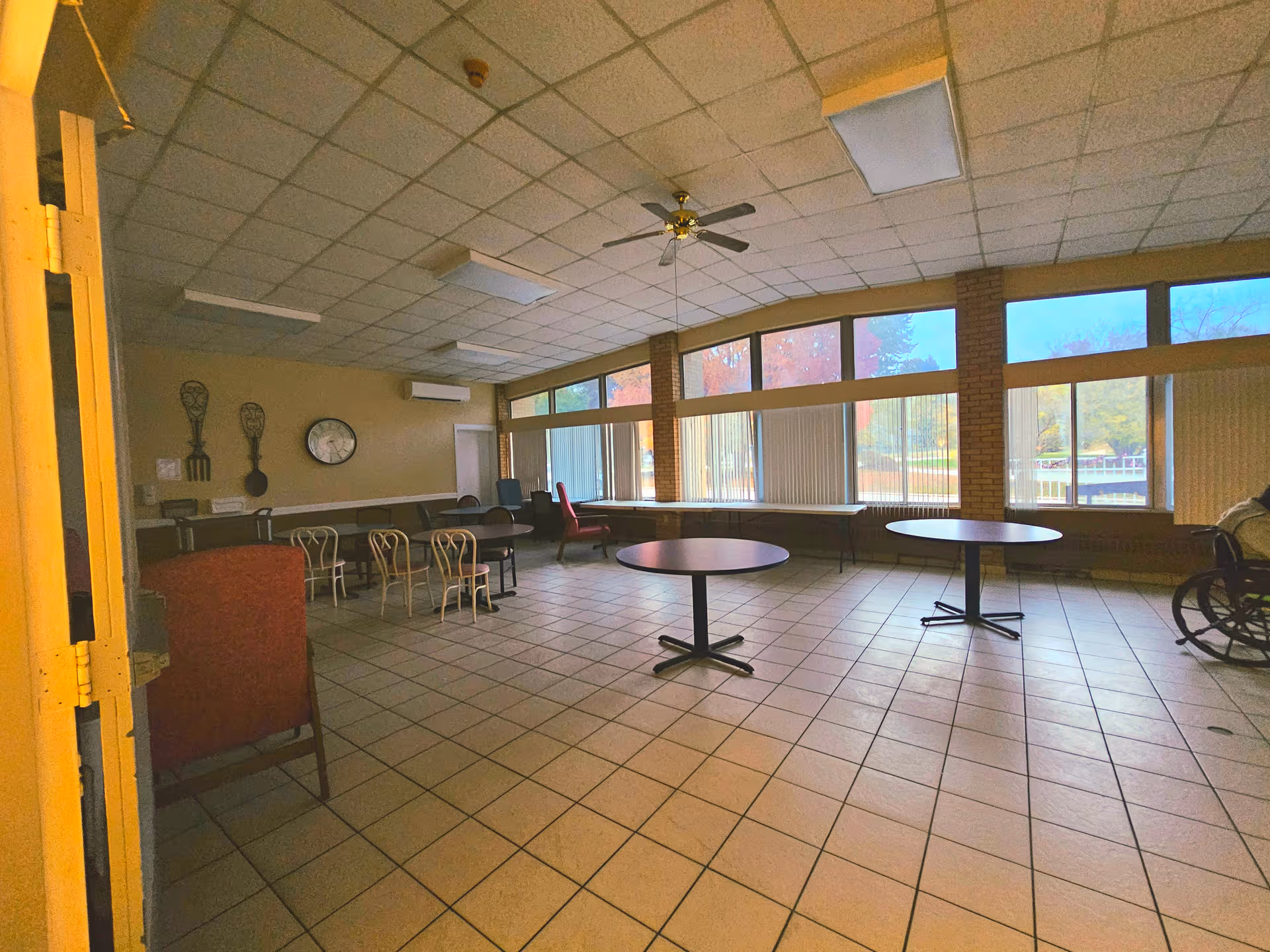 Spacious common room with round tables, chairs, tiled floor, and large windows.