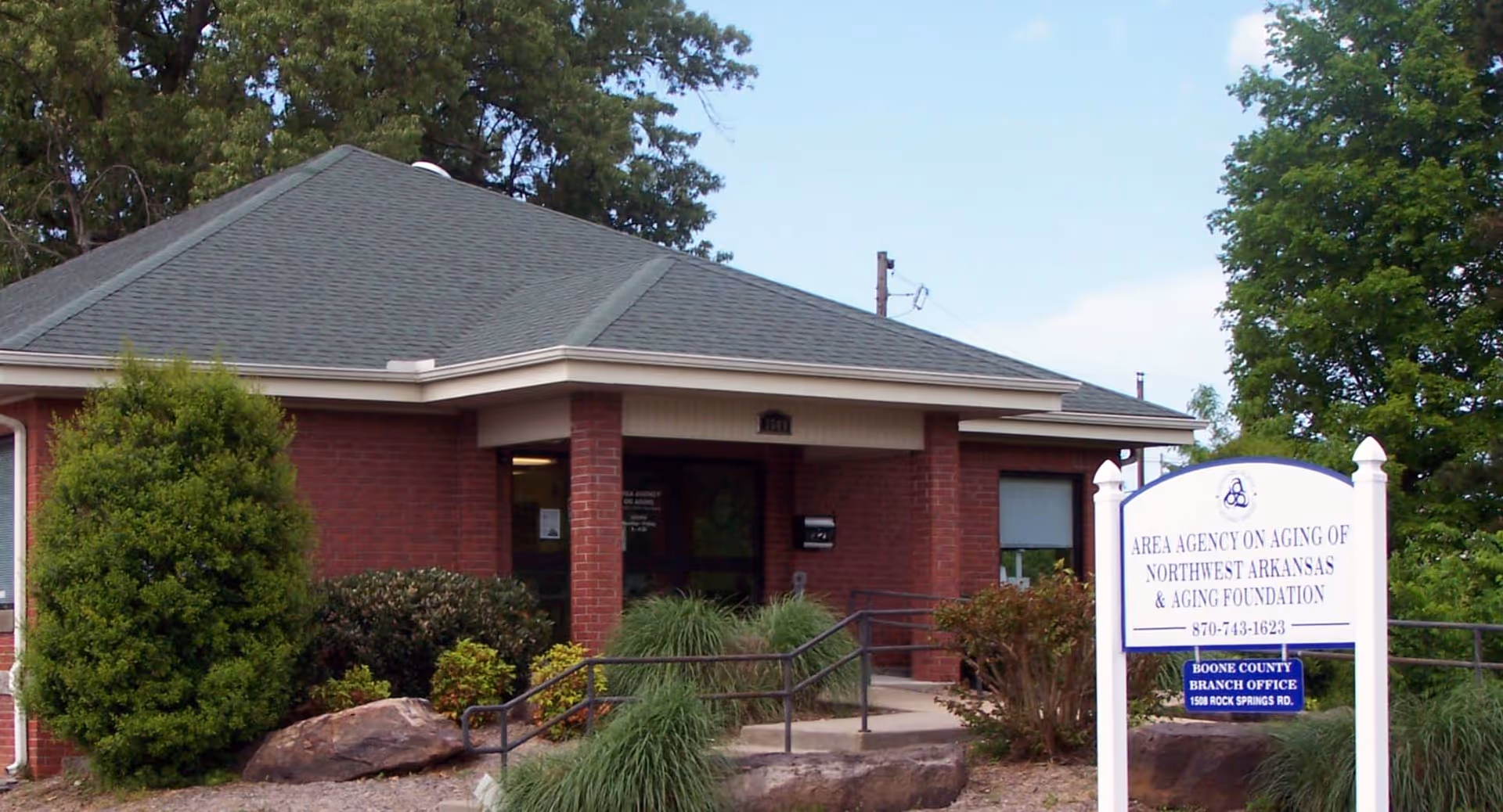 Brick building with a covered entrance and a sign in the front yard.