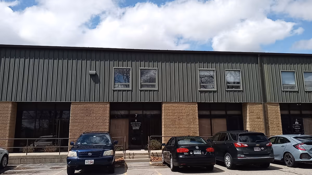 Front view of a two-tone brick and metal storefront with parked cars.