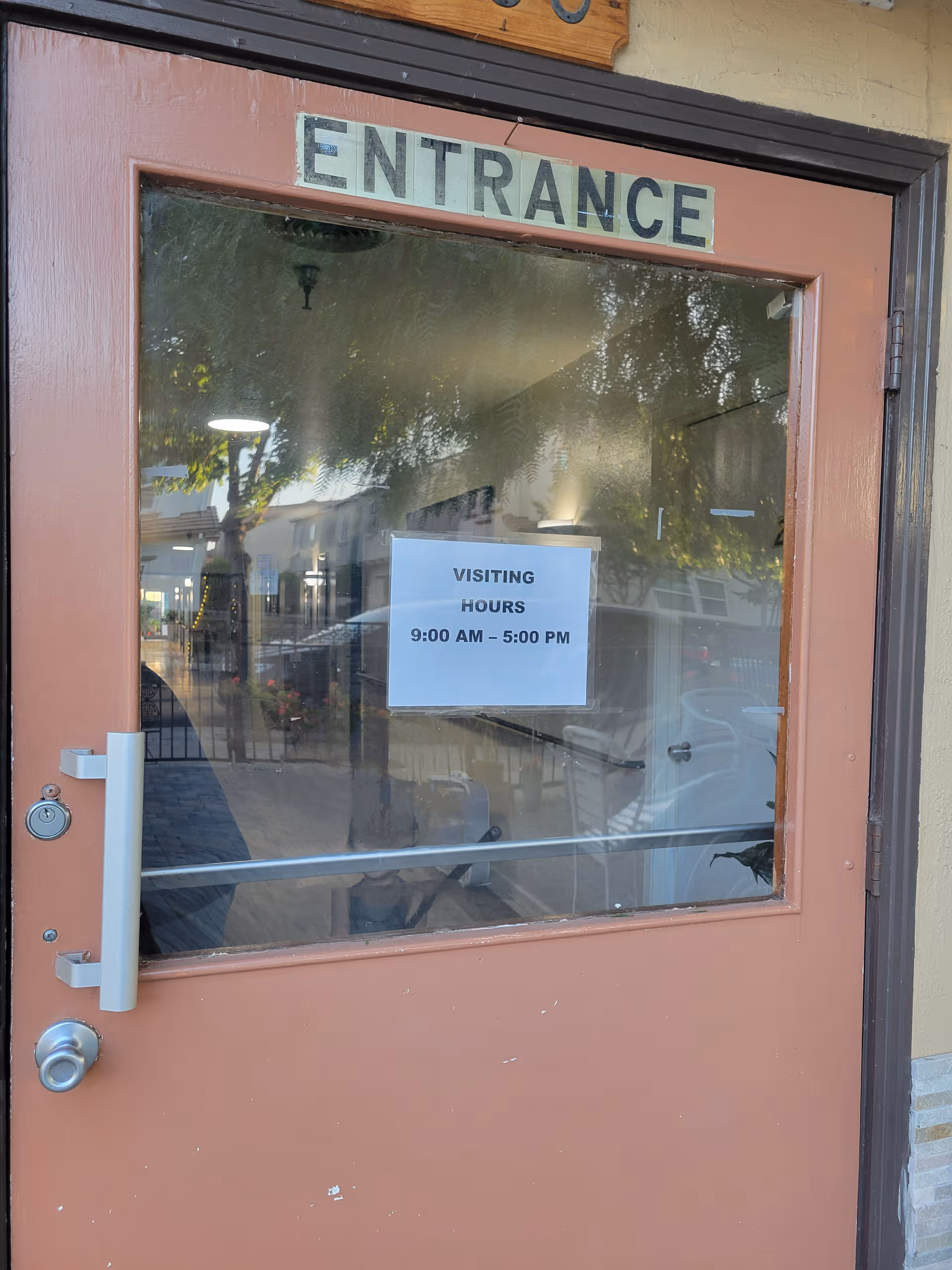 Brown entrance door with ENTRANCE sign and posted visiting hours notice