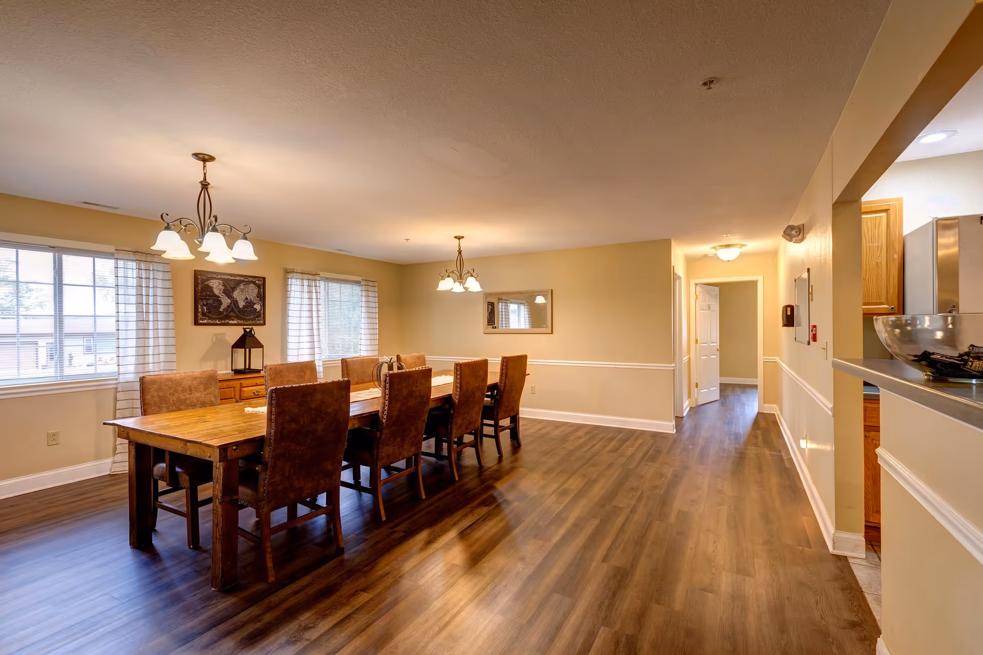 Spacious dining room with a long wooden table, chairs, and warm overhead lighting.