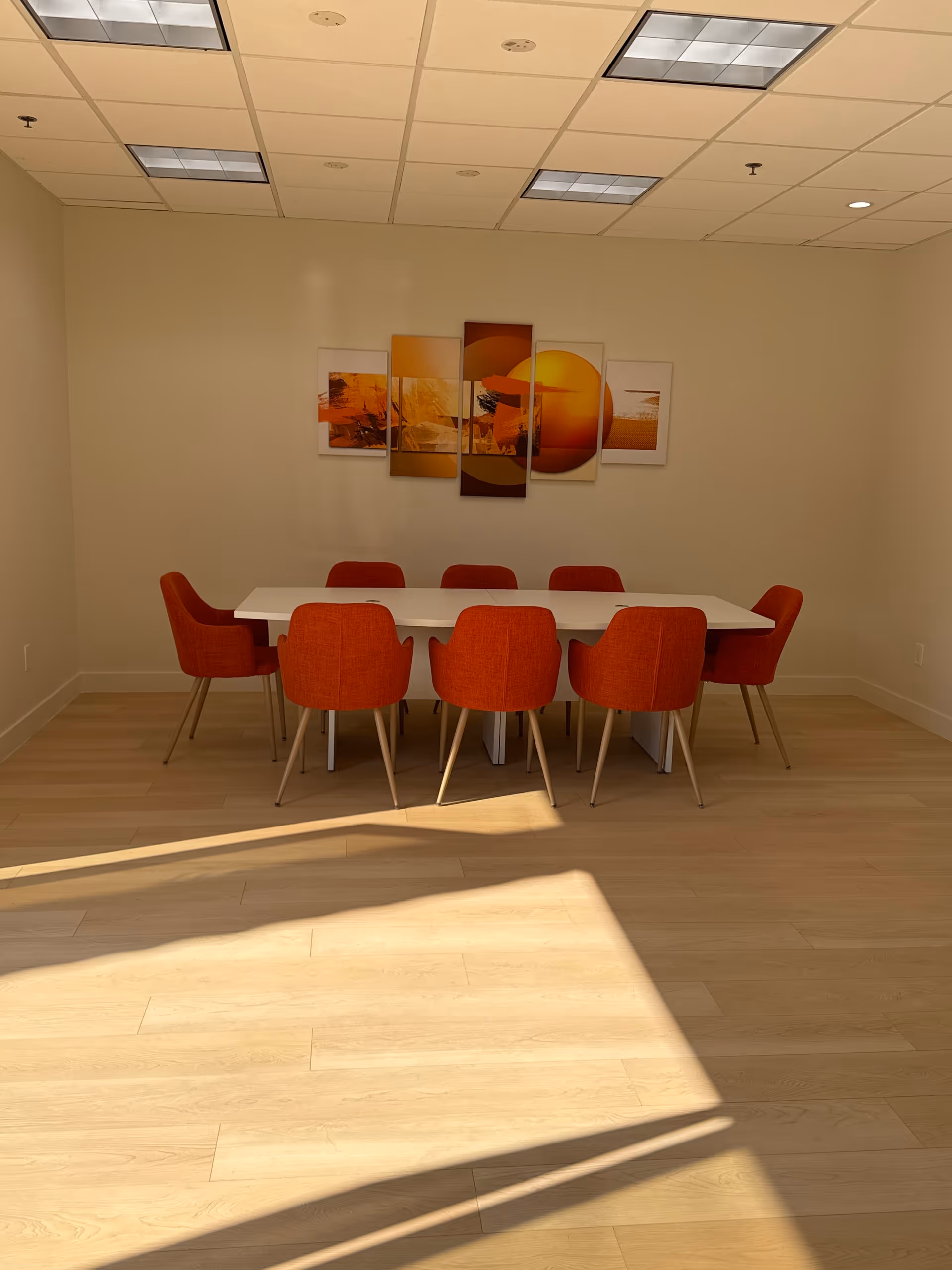 A bright dining room with a white table and red-orange chairs under ceiling lights.