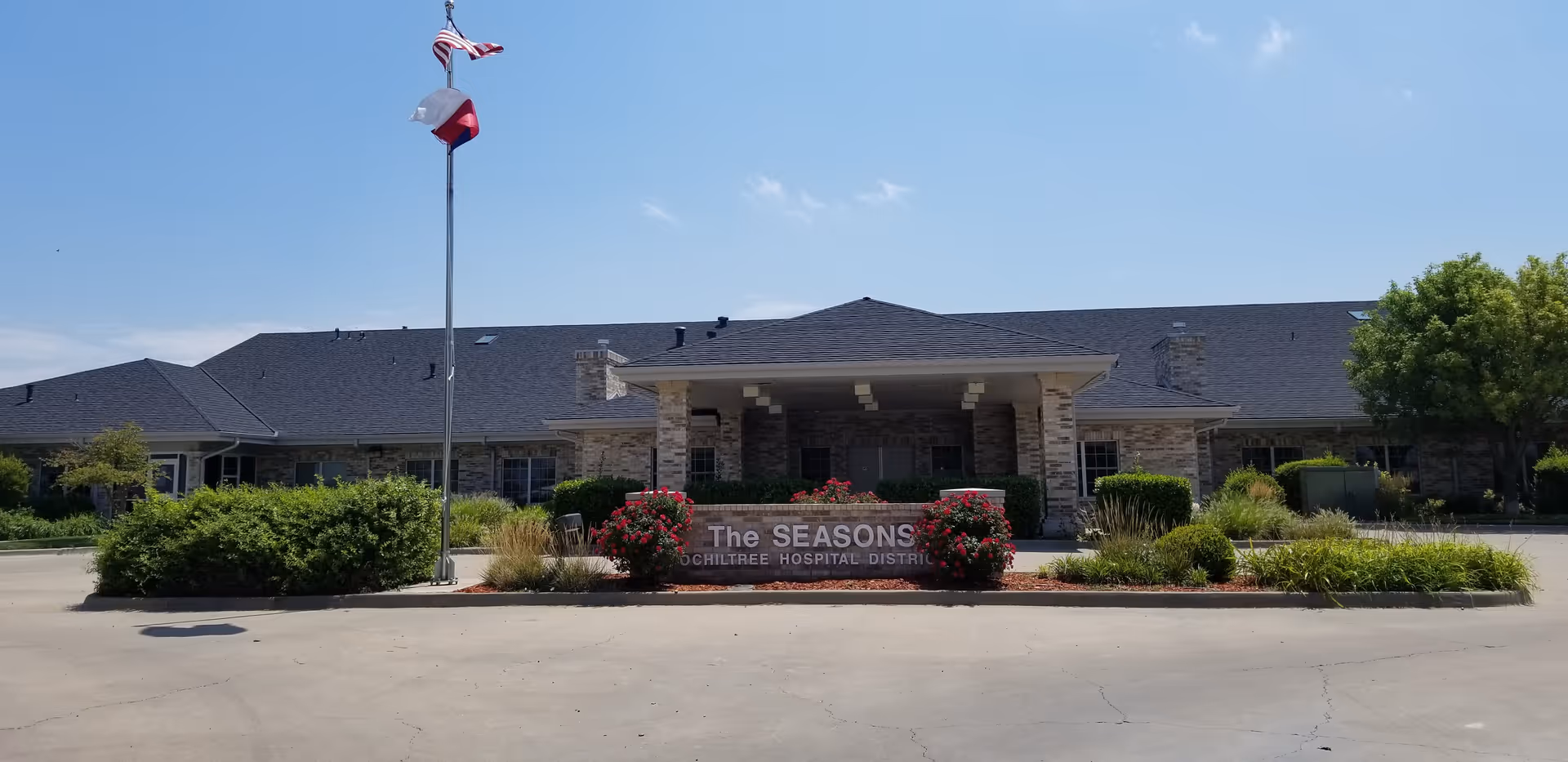 Front view of The Seasons Assisted Living facility with flagpole and landscaped entrance.
