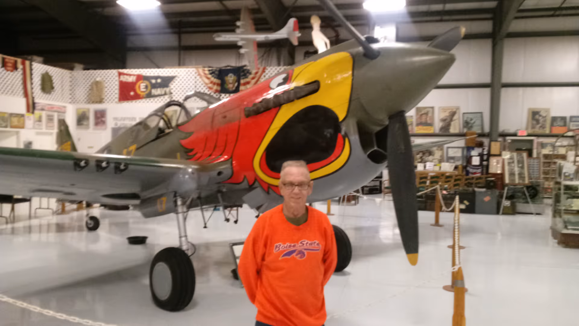 Indoor aircraft museum with a parked vintage plane and a man in orange sweatshirt.