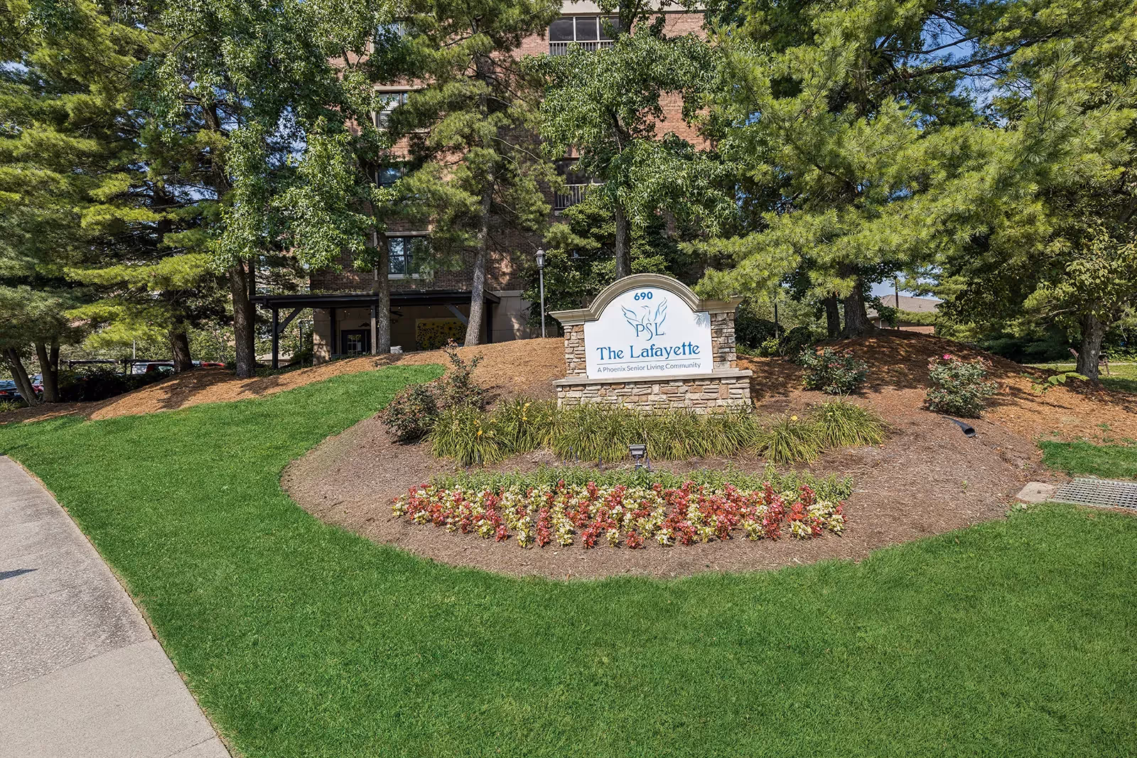 The Lafayette senior living community sign sits amid trimmed flower beds and trees at front.