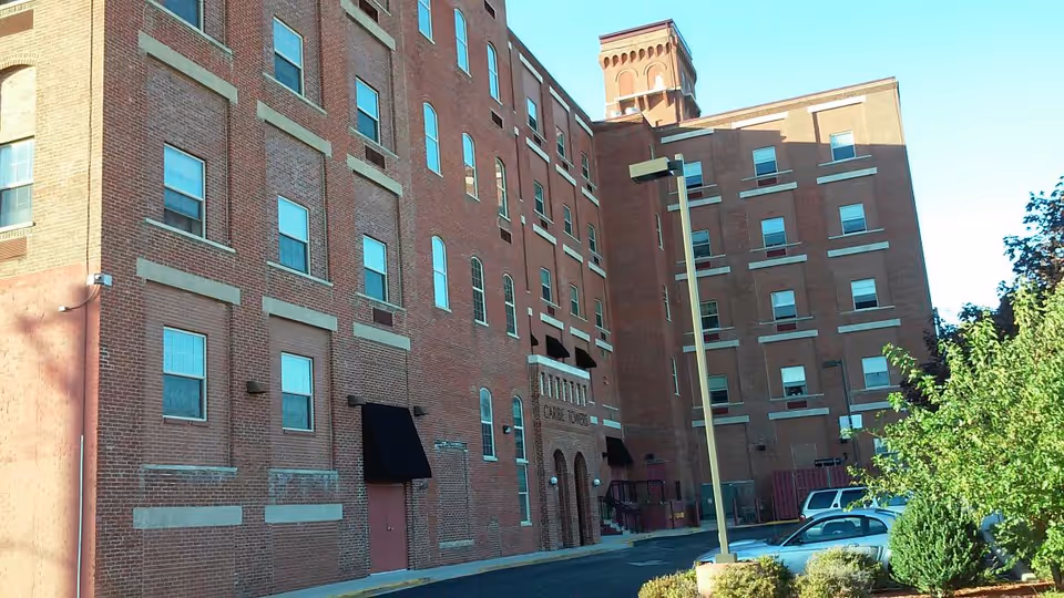 Brick multi-story building exterior with arched windows and entrance beneath a clear blue sky.