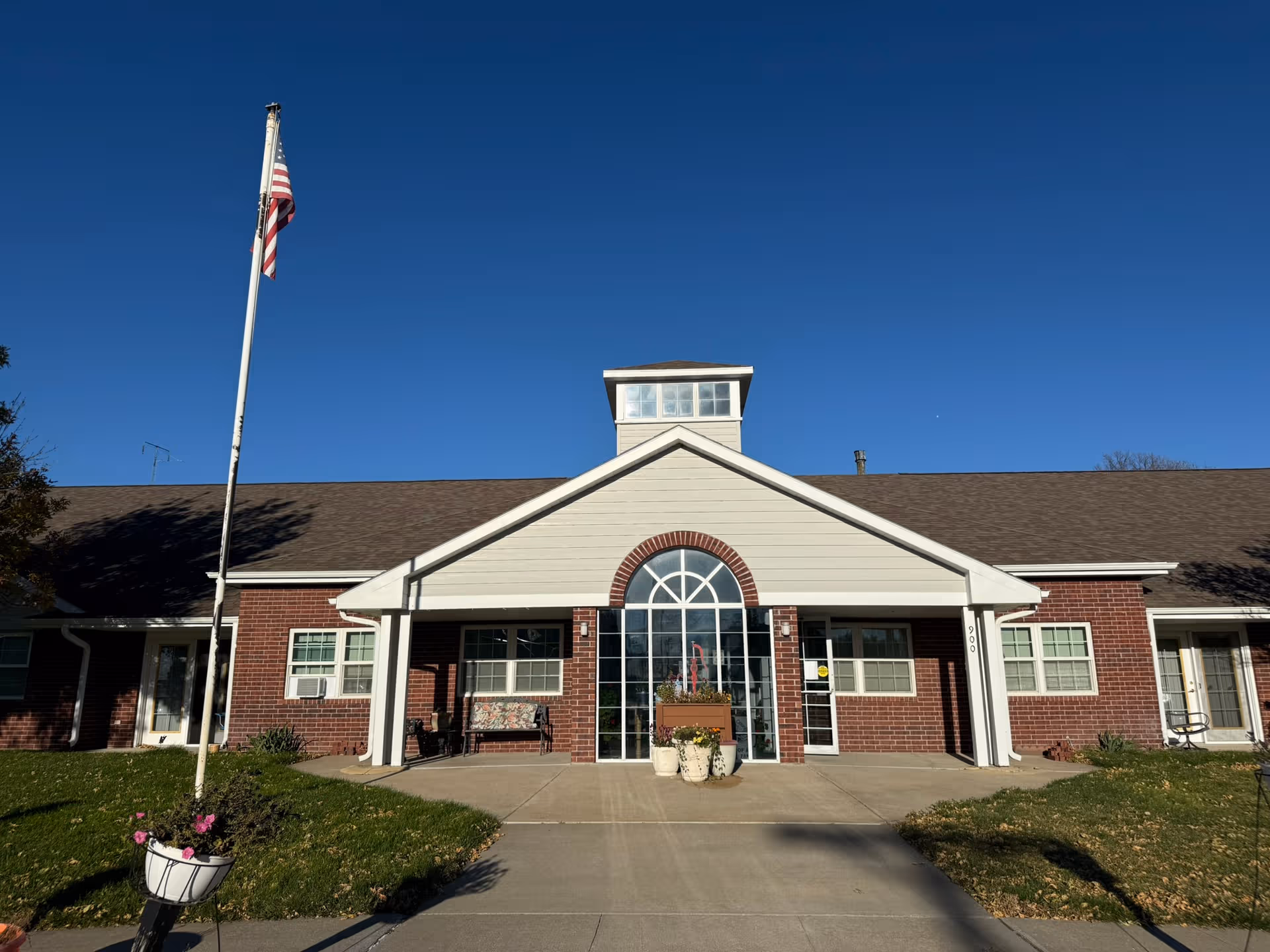 Front exterior of a brick senior living facility with flagpole and glass entrance.