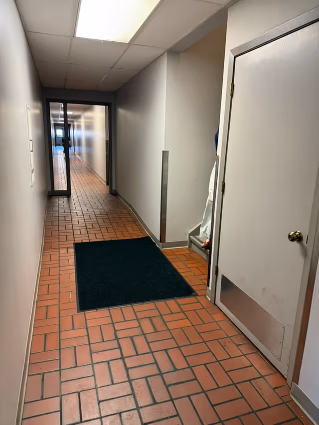 A long interior hallway of a senior living facility with tiled flooring and a glass door.