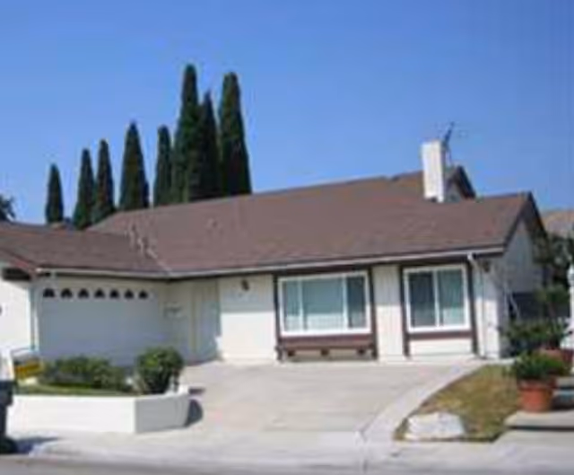 Single-story beige residential building with brown roof, driveway, and minimal landscaping.