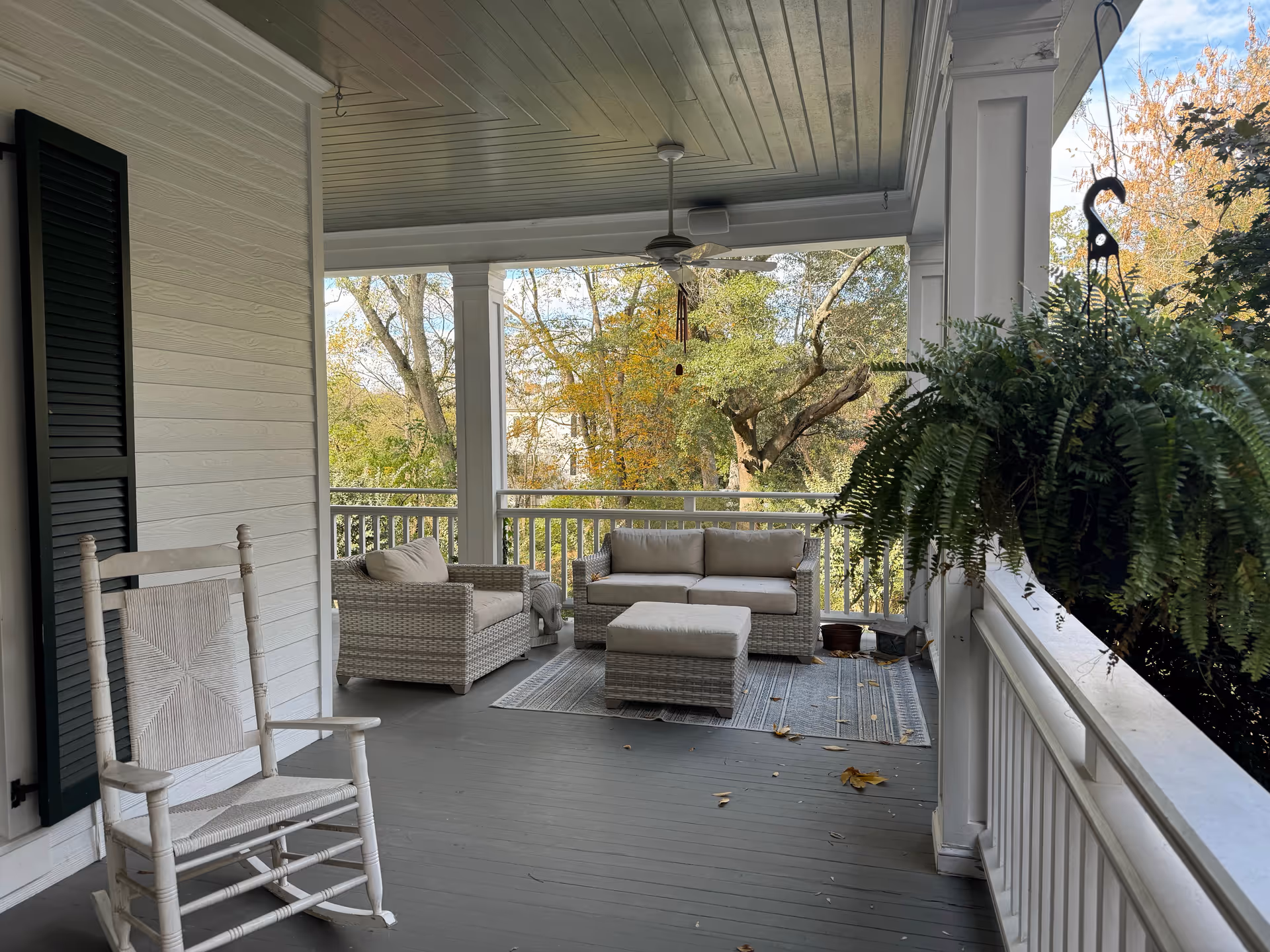 Covered porch with wicker furniture, a fern, and fall foliage view.