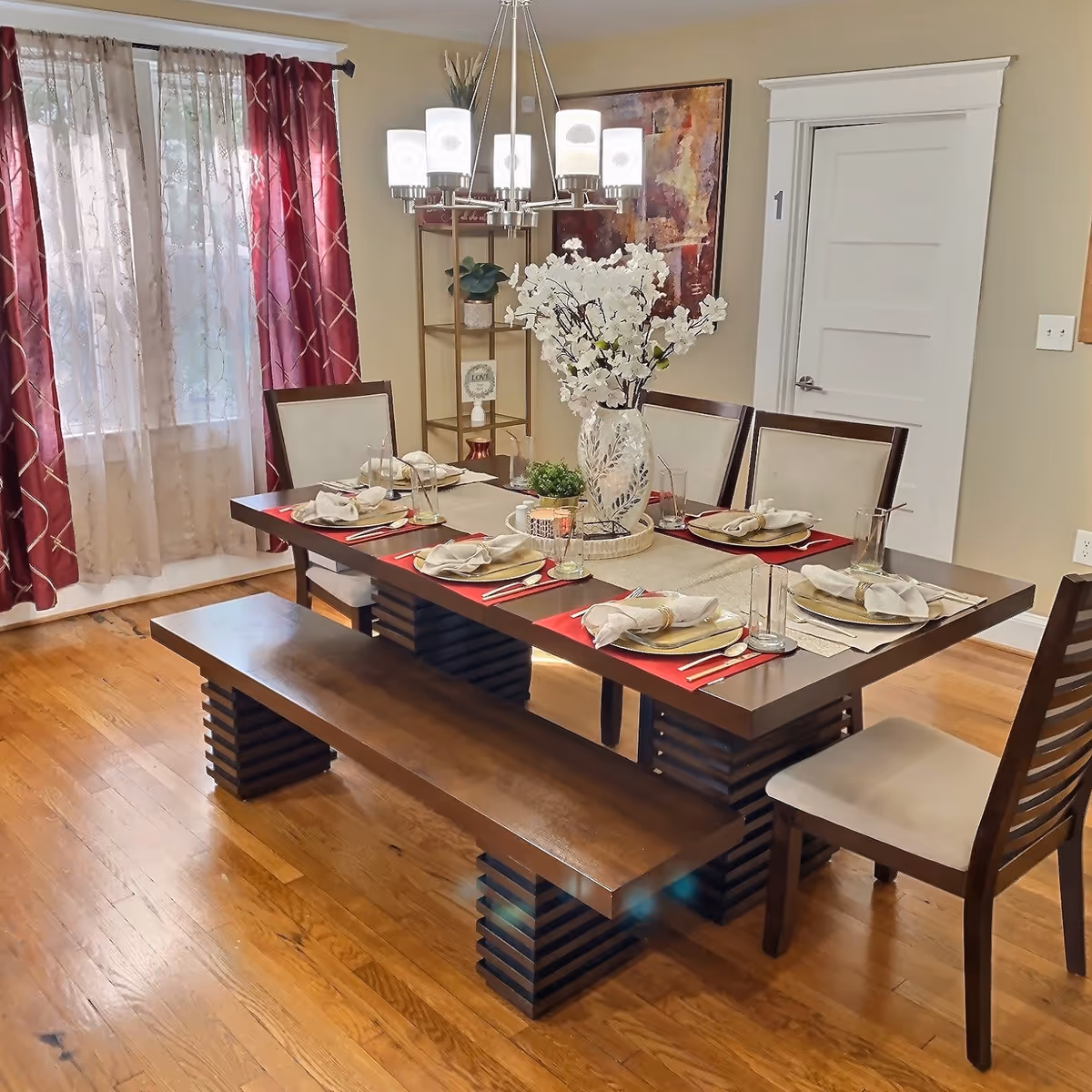 A well-lit dining room featuring a long table, bench seating, and a centerpiece.