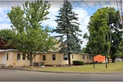 Front view of a single-story tan care facility with trees by the street.