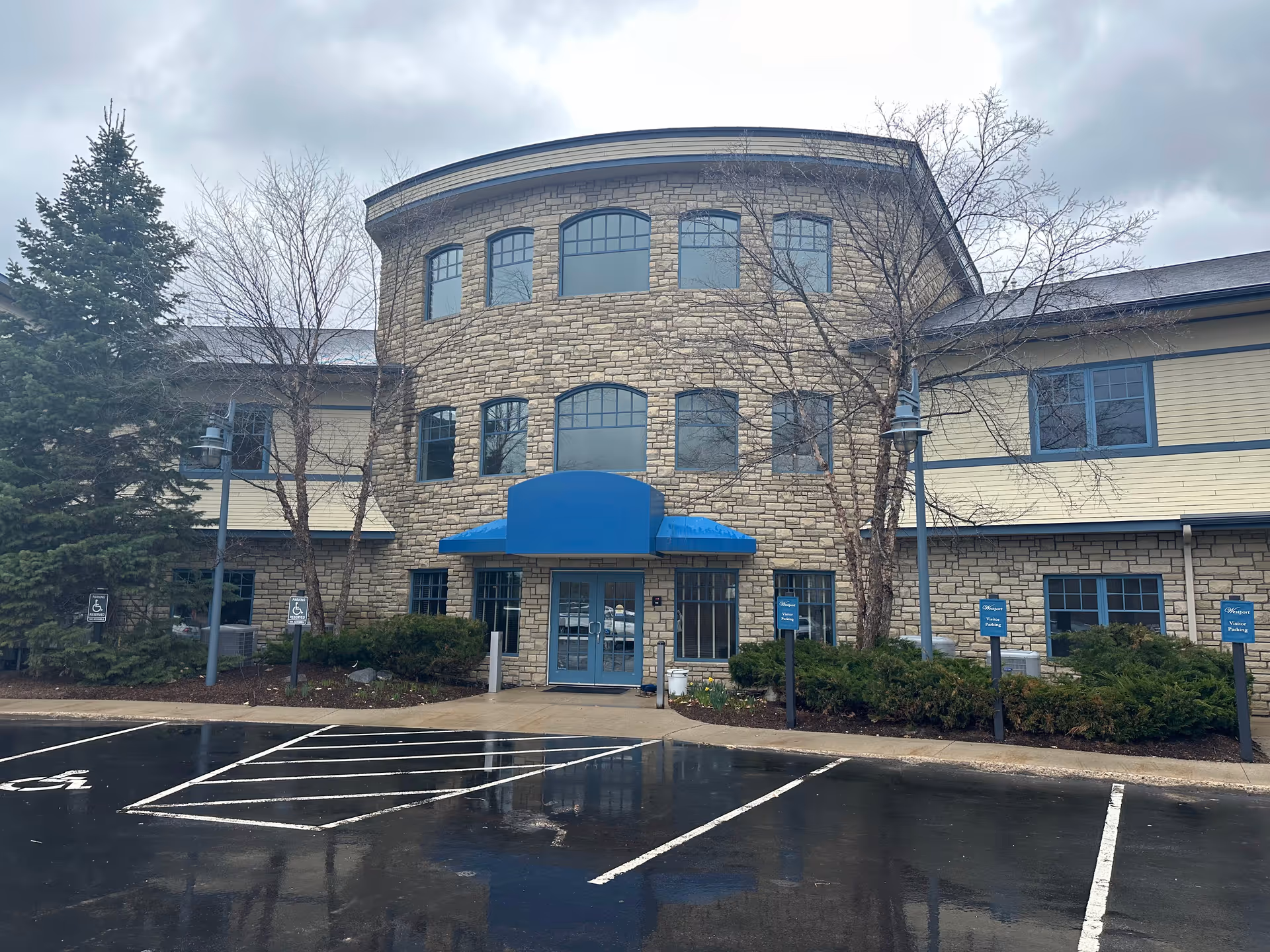 Stone and beige facility exterior with a blue entrance awning and parking.