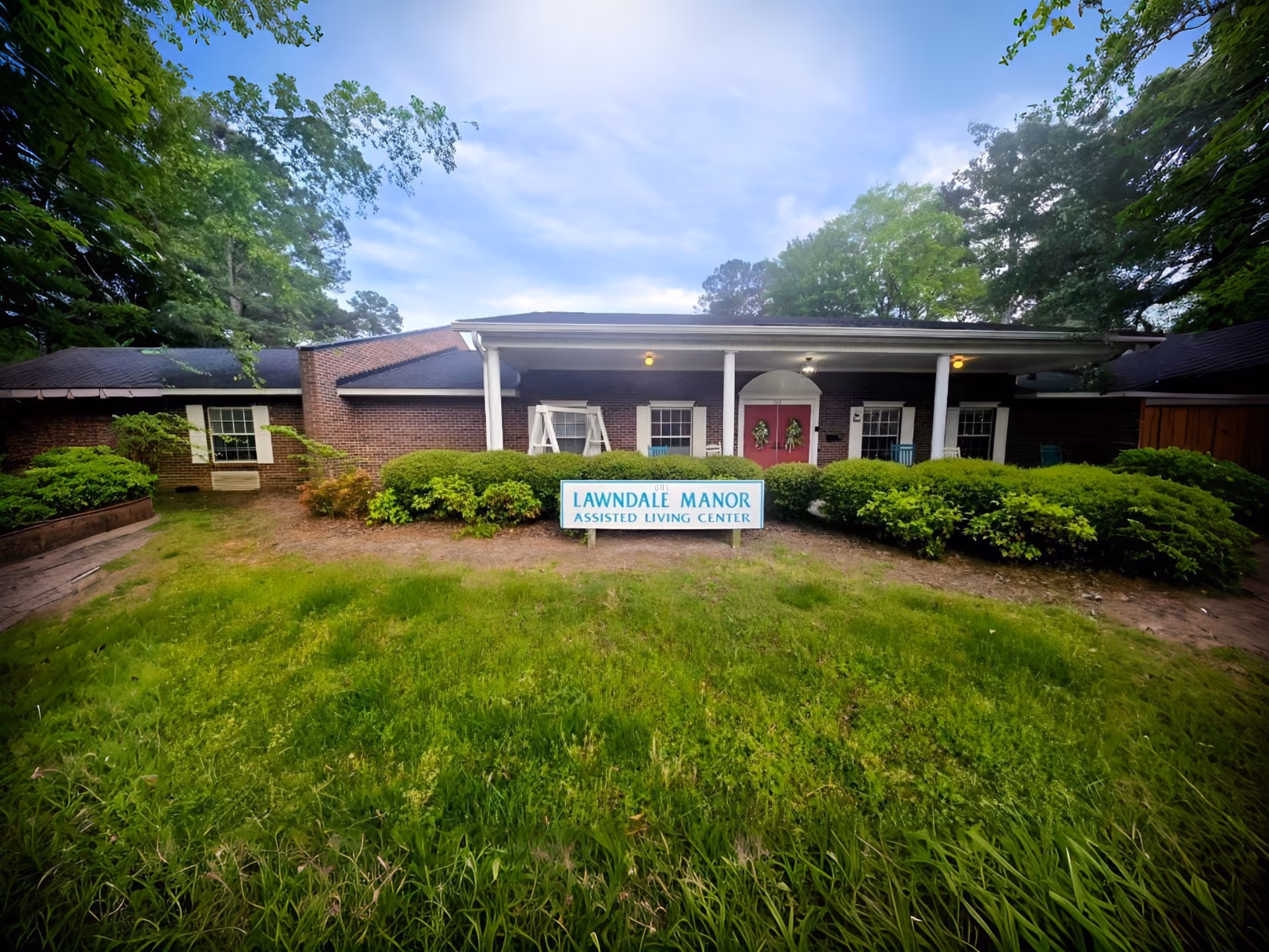 Brick assisted-living facility with white columns and a Lawndale Manor sign, surrounded by greenery.