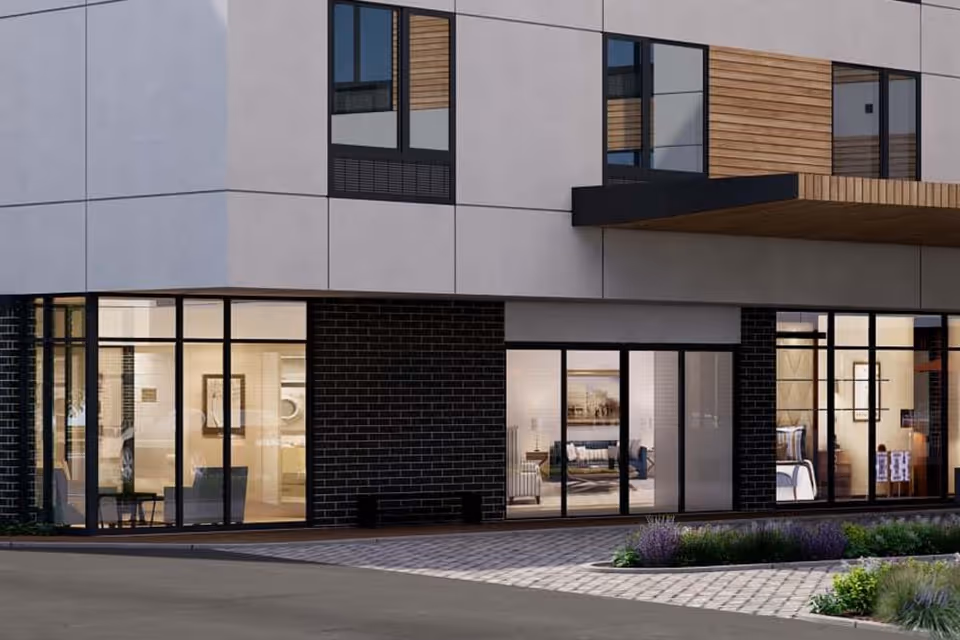 Modern senior living building facade with large ground-floor windows revealing furnished interior lounges and apartments.