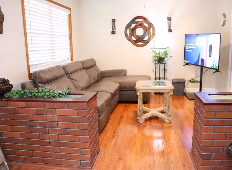 A cozy living room in a senior facility with a brown sectional sofa and brick planters.