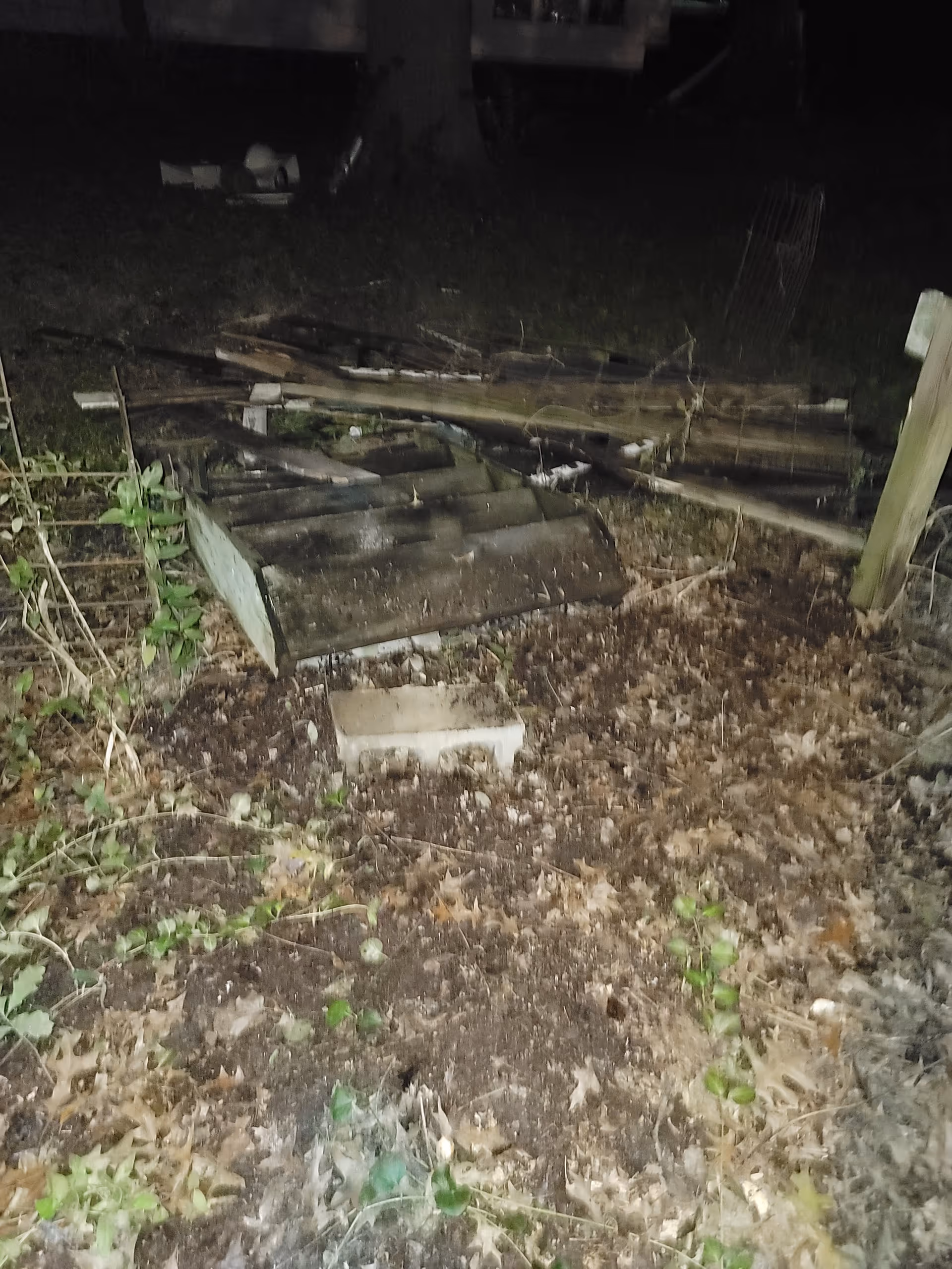 Nighttime outdoor area with scattered wood, debris, and concrete blocks on muddy ground.
