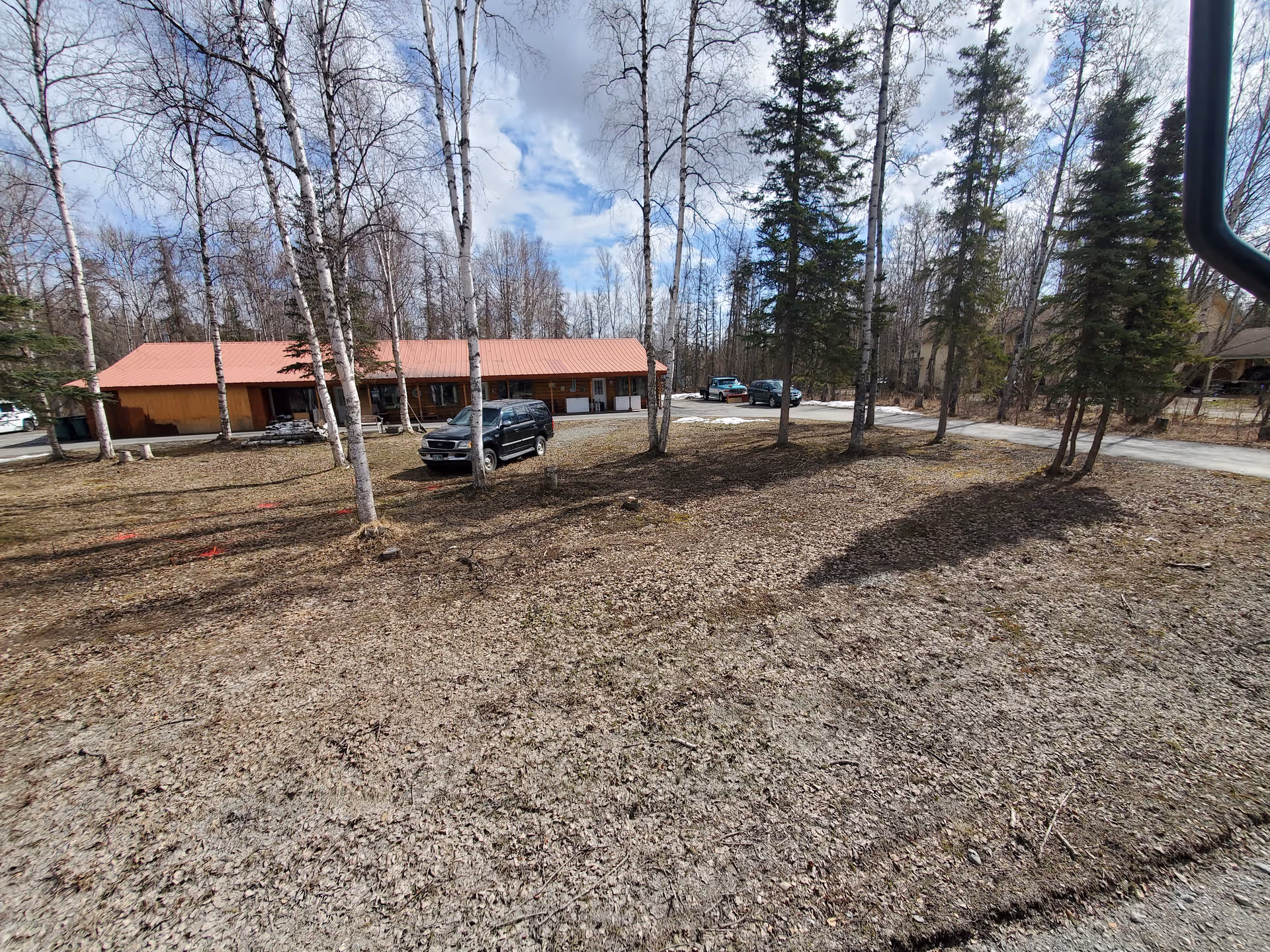 A single-story building with a red roof sits among leafless trees and parked cars.