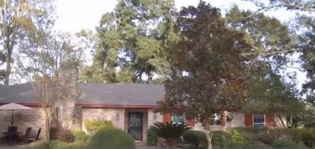 Single-story care home exterior with entrance, trees, and outdoor seating.