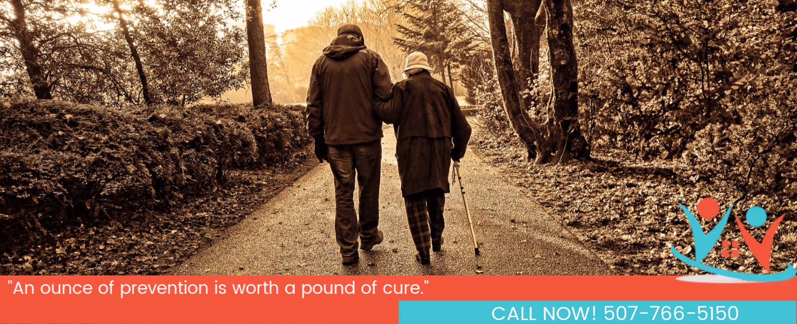 Two elderly individuals walk hand-in-hand along a tree-lined outdoor path in autumn.