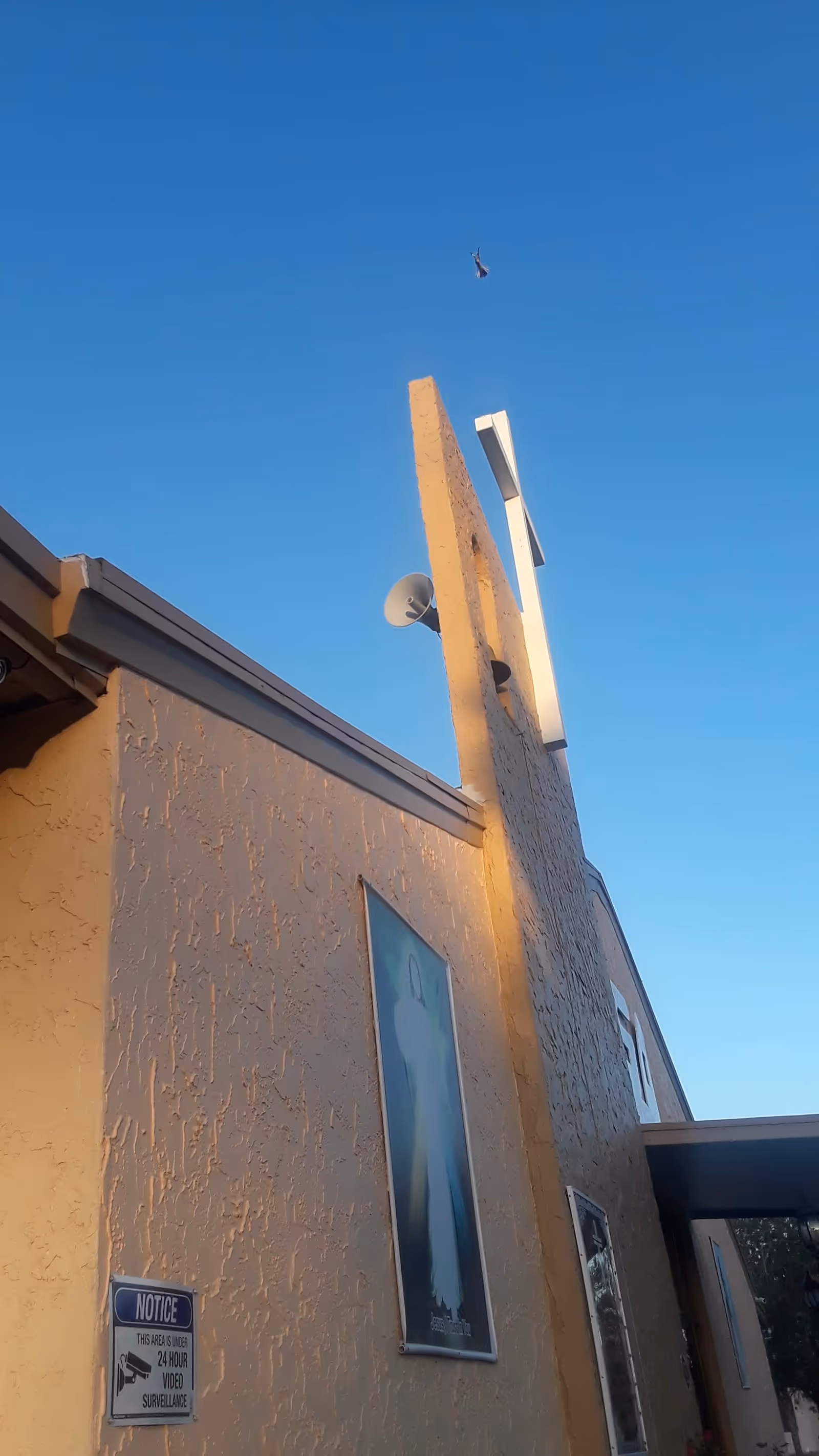 Beige stucco building exterior with a satellite dish and posters against a blue sky.