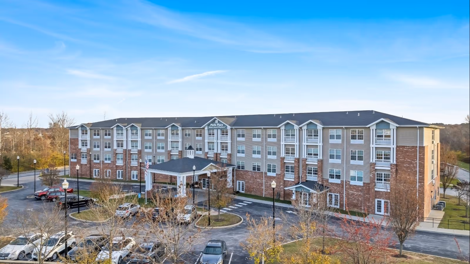 A multi-story senior living facility exterior with a front entrance, parking, and surrounding trees.