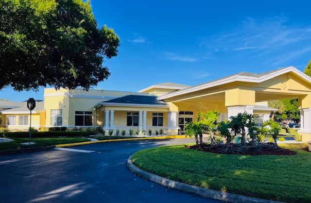 Exterior of a yellow senior living facility with a curved driveway and covered entrance.